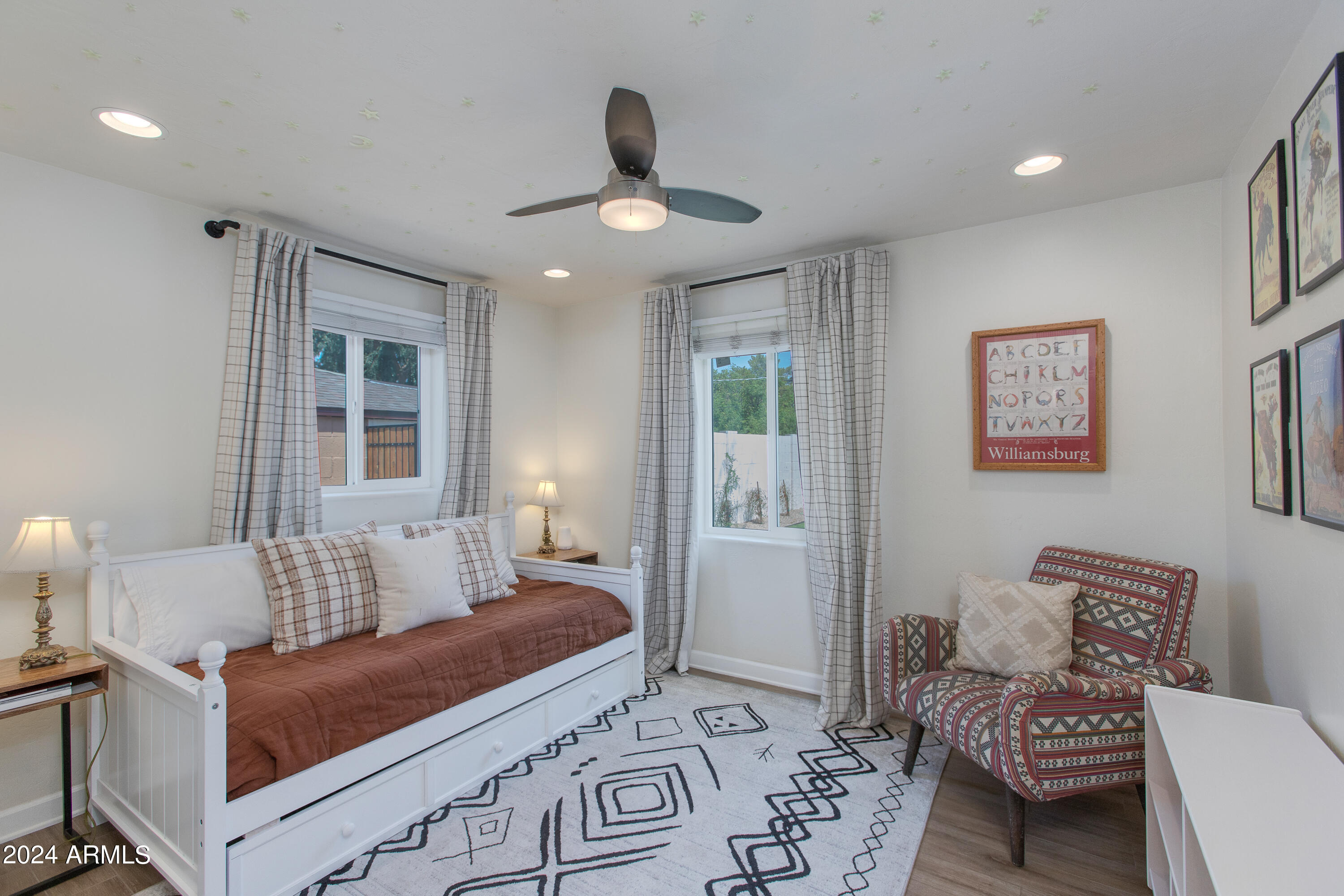 Bedroom with a white daybed, rust-colored bedding, curtained windows, and a patterned armchair.