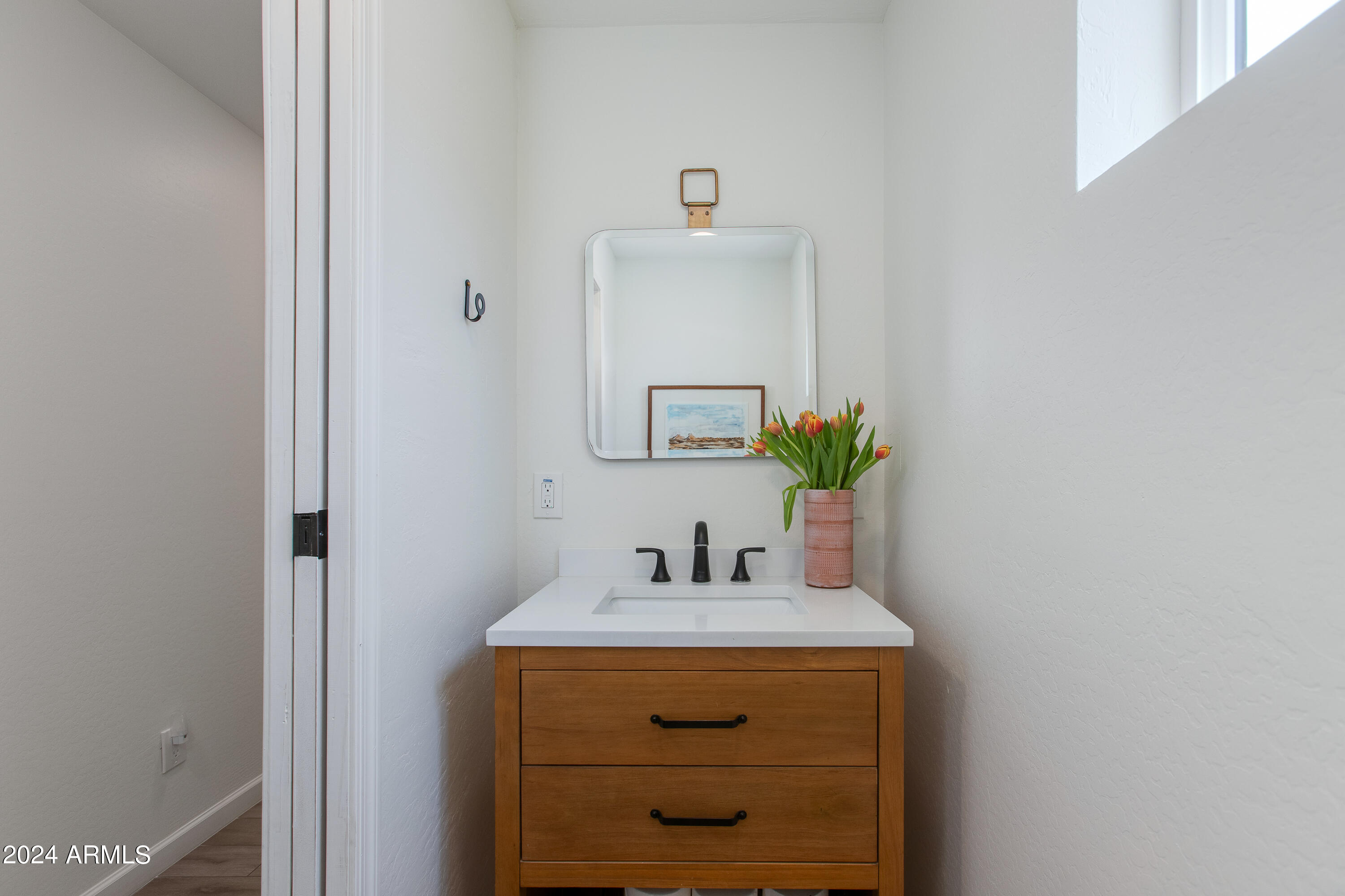 Bathroom vanity with a wood cabinet, white sink, black faucet, and tulips beside a mirror.