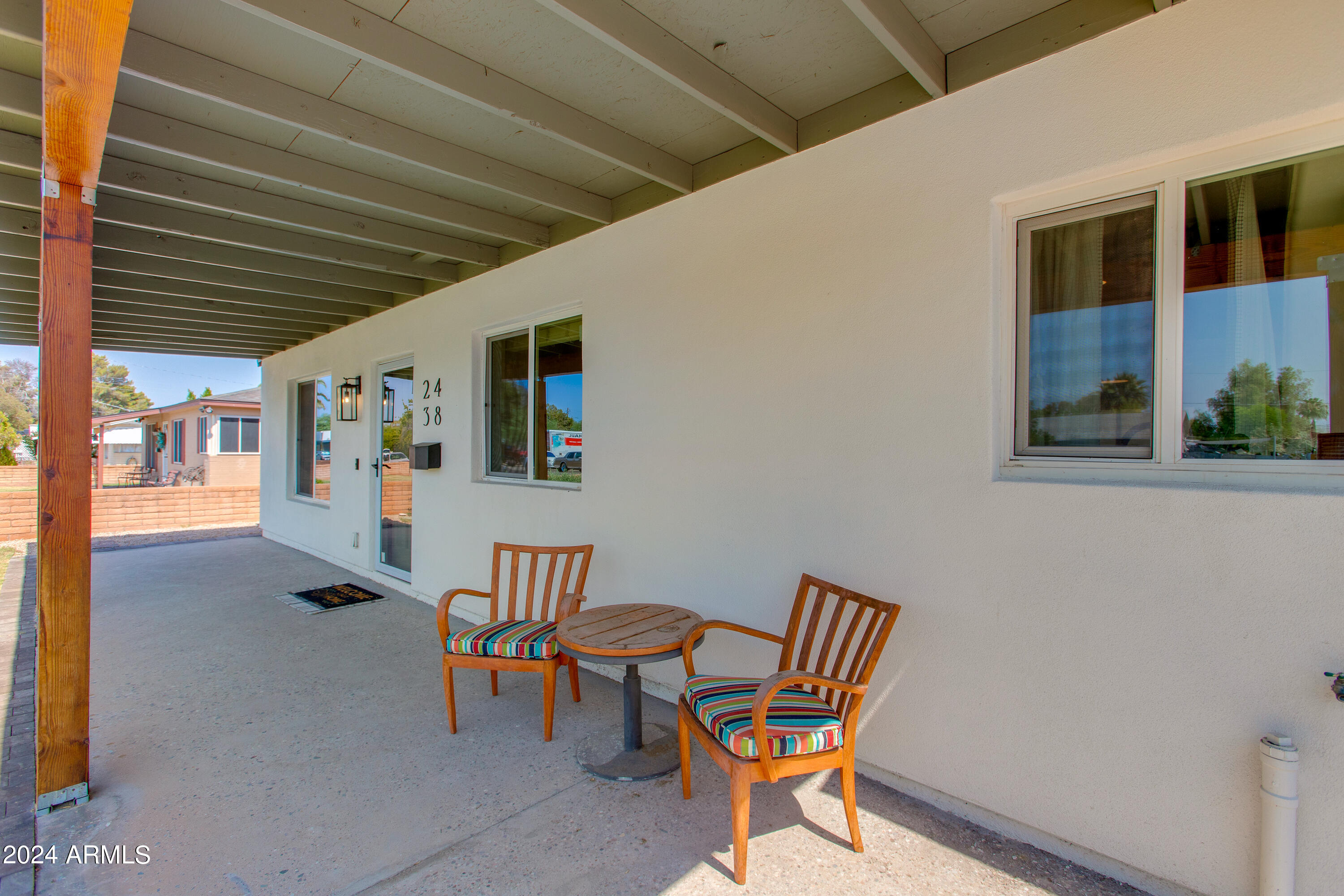 Covered front porch with two colorful cushioned chairs and a small table beside the entry.