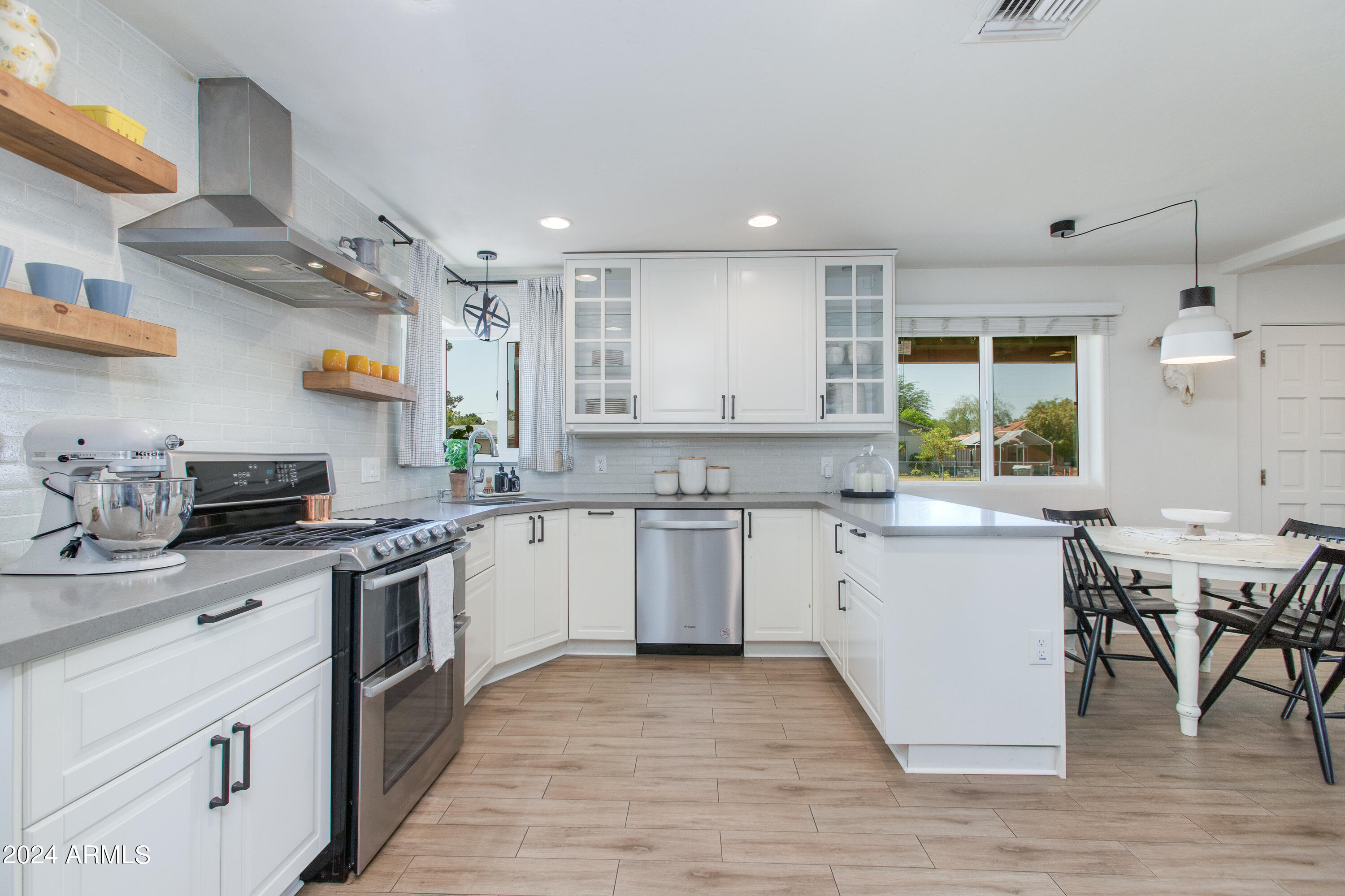 Bright white kitchen with stainless steel appliances, open wood shelves, and a peninsula beside the dining area.