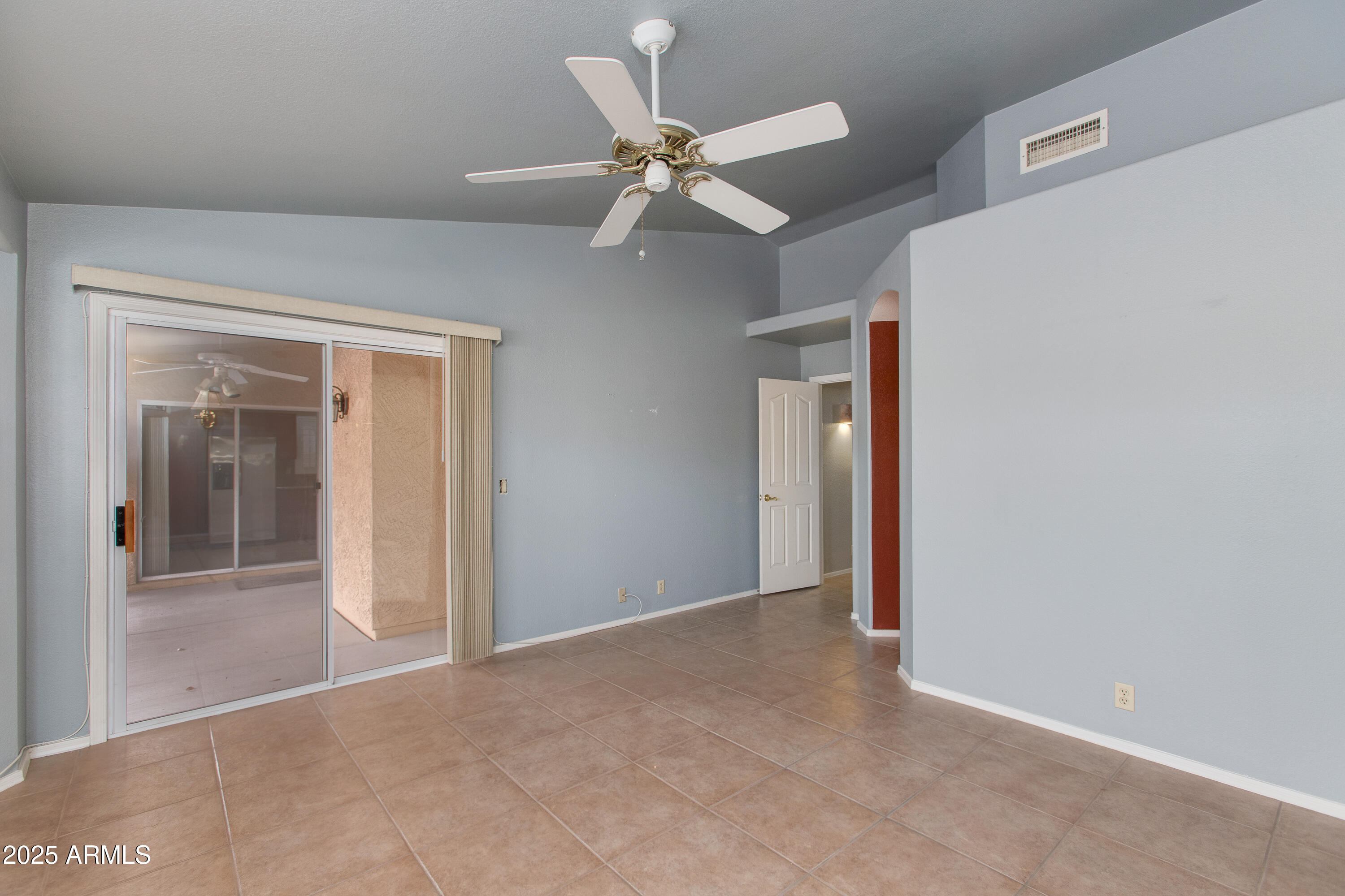 Empty tiled room with a ceiling fan and sliding glass door to a covered patio.