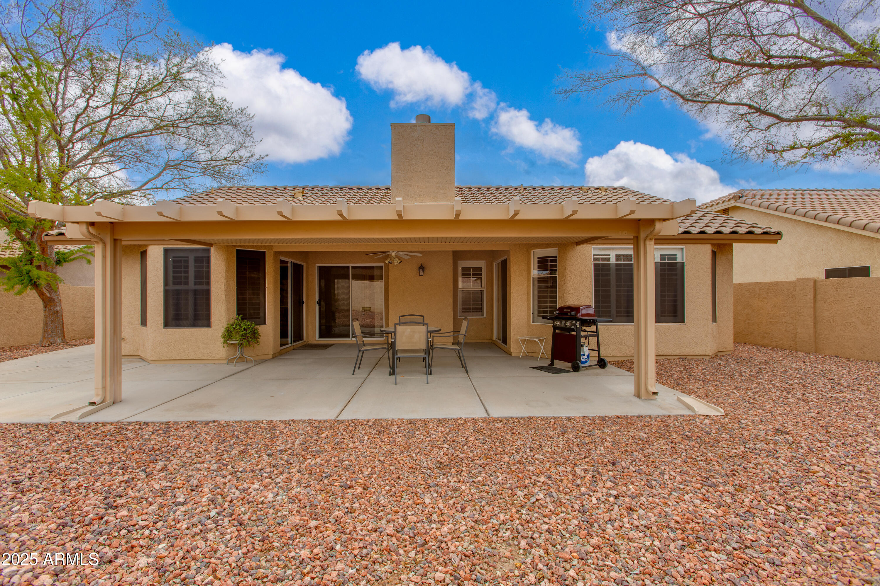 Home’s covered rear patio with outdoor dining furniture, barbecue grill, and gravel landscaping.