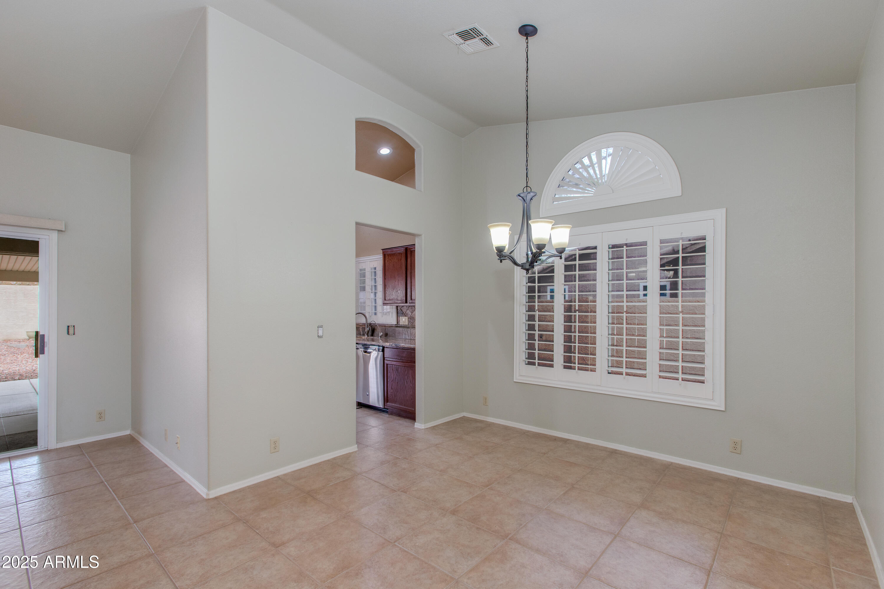 Empty dining area with tiled floors, chandelier, and a large arched window with shutters.