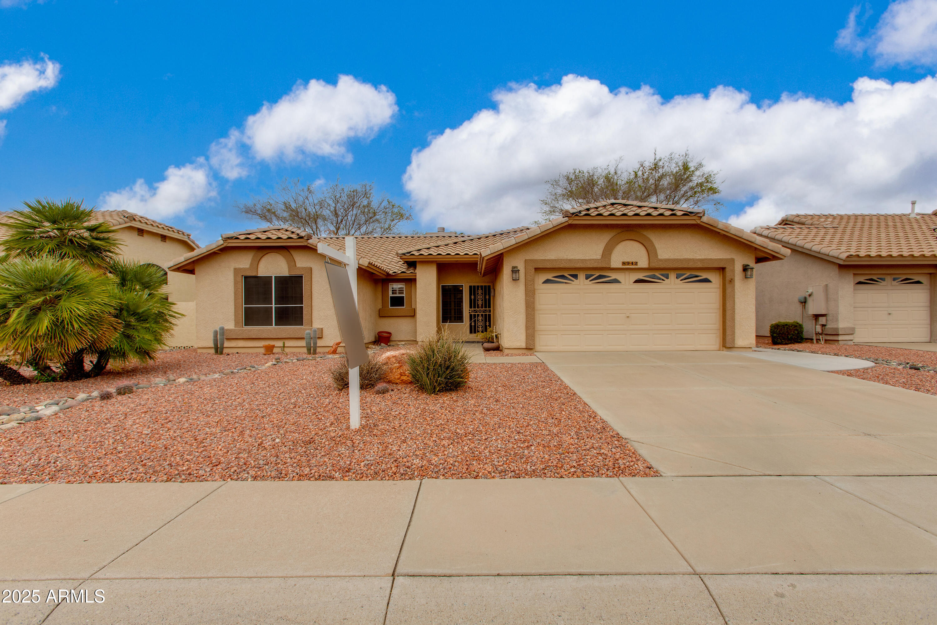 Single-story stucco home with a tile roof, two-car garage, and desert rock landscaping.