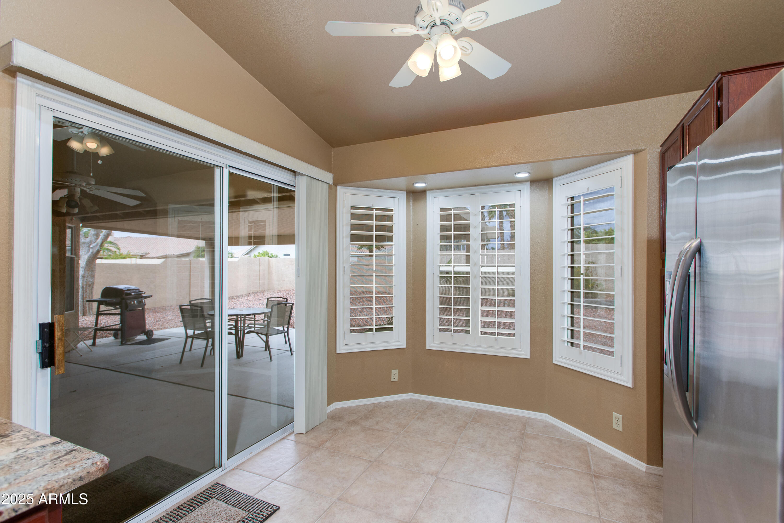 Kitchen eating area with plantation shutters, stainless steel refrigerator, and sliding glass door to a covered patio.