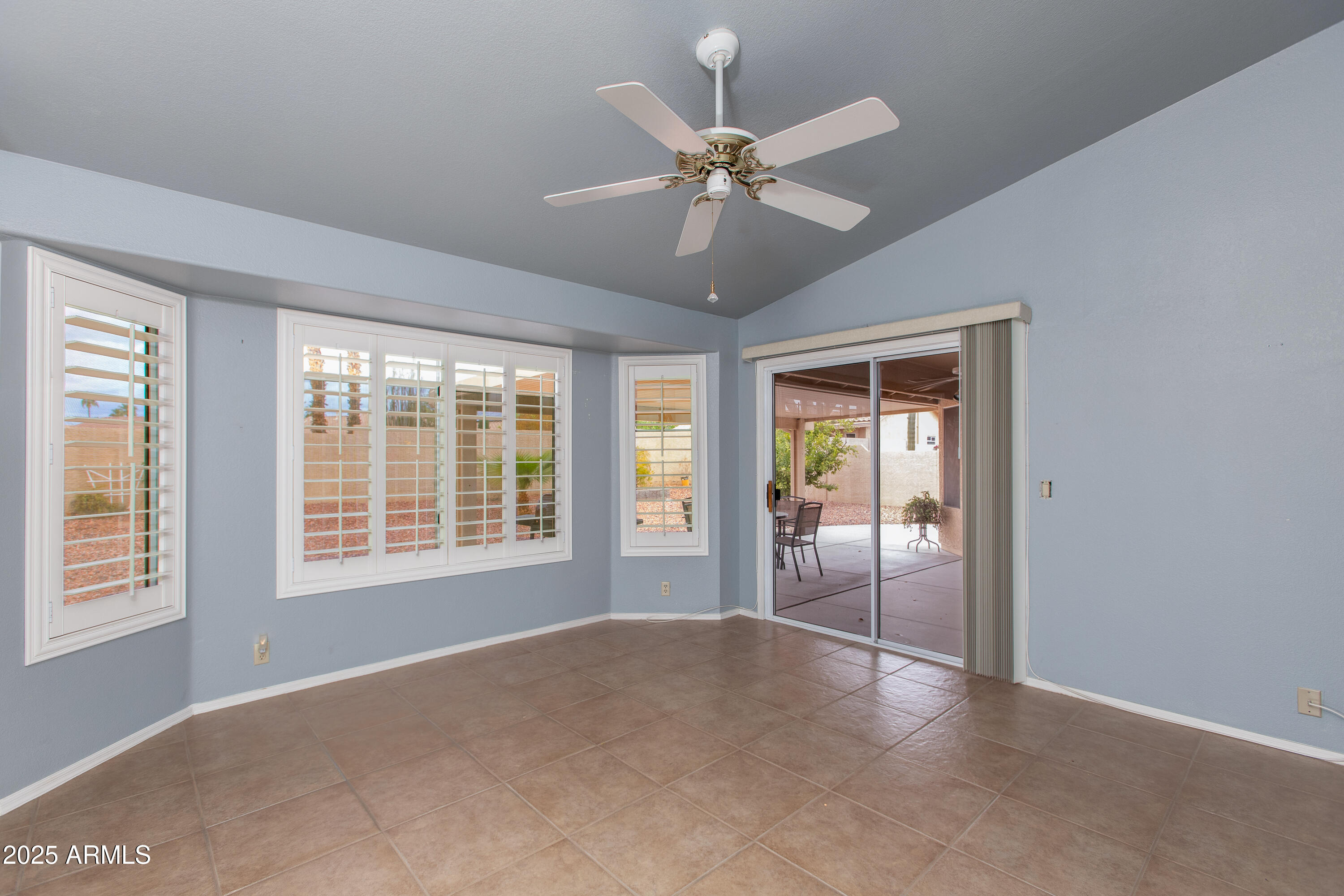 Vacant tiled room with plantation shutters, a ceiling fan, and sliding glass doors to a covered patio.
