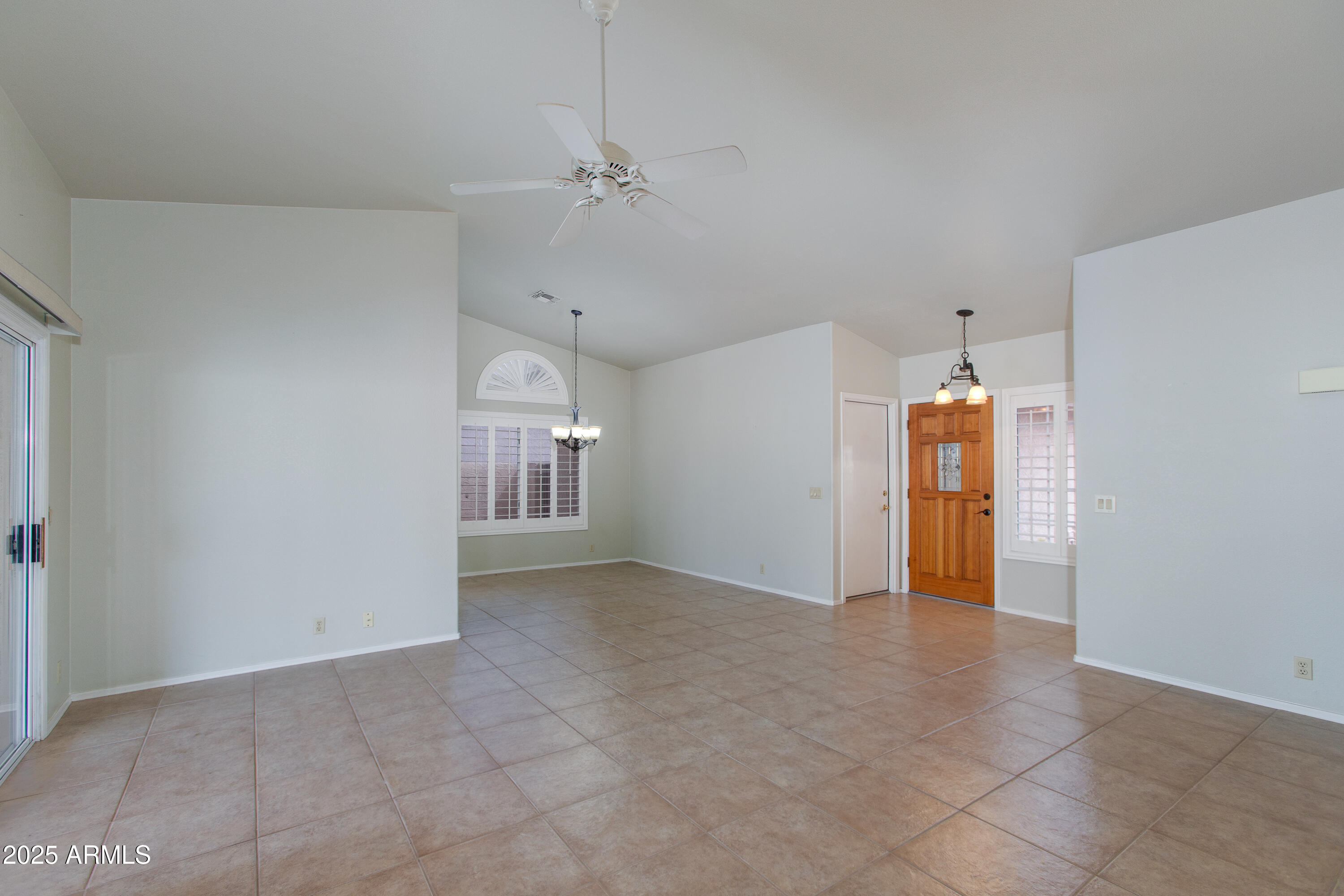 Vacant living and dining area with tile floors, shuttered windows, and a wooden front door.