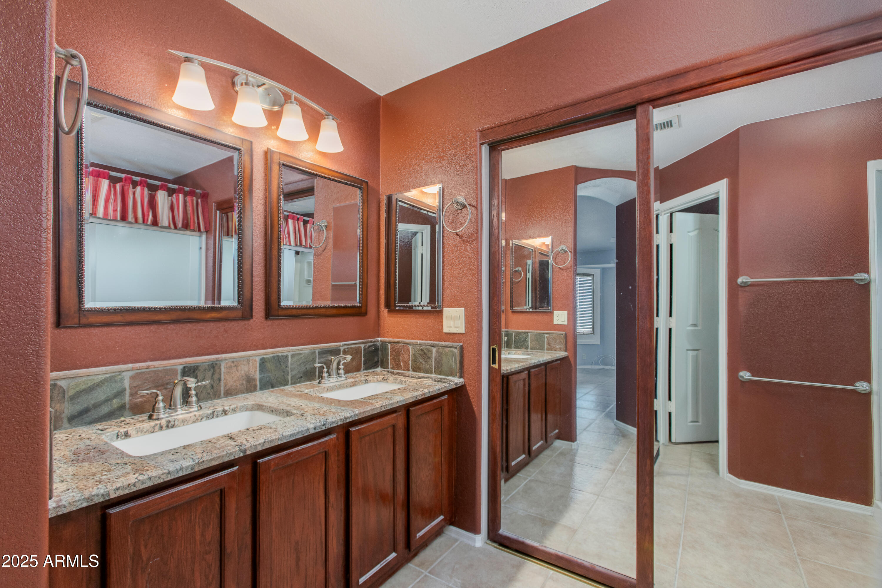 Bathroom with a double-sink granite vanity, dark wood cabinets, and multiple framed mirrors.