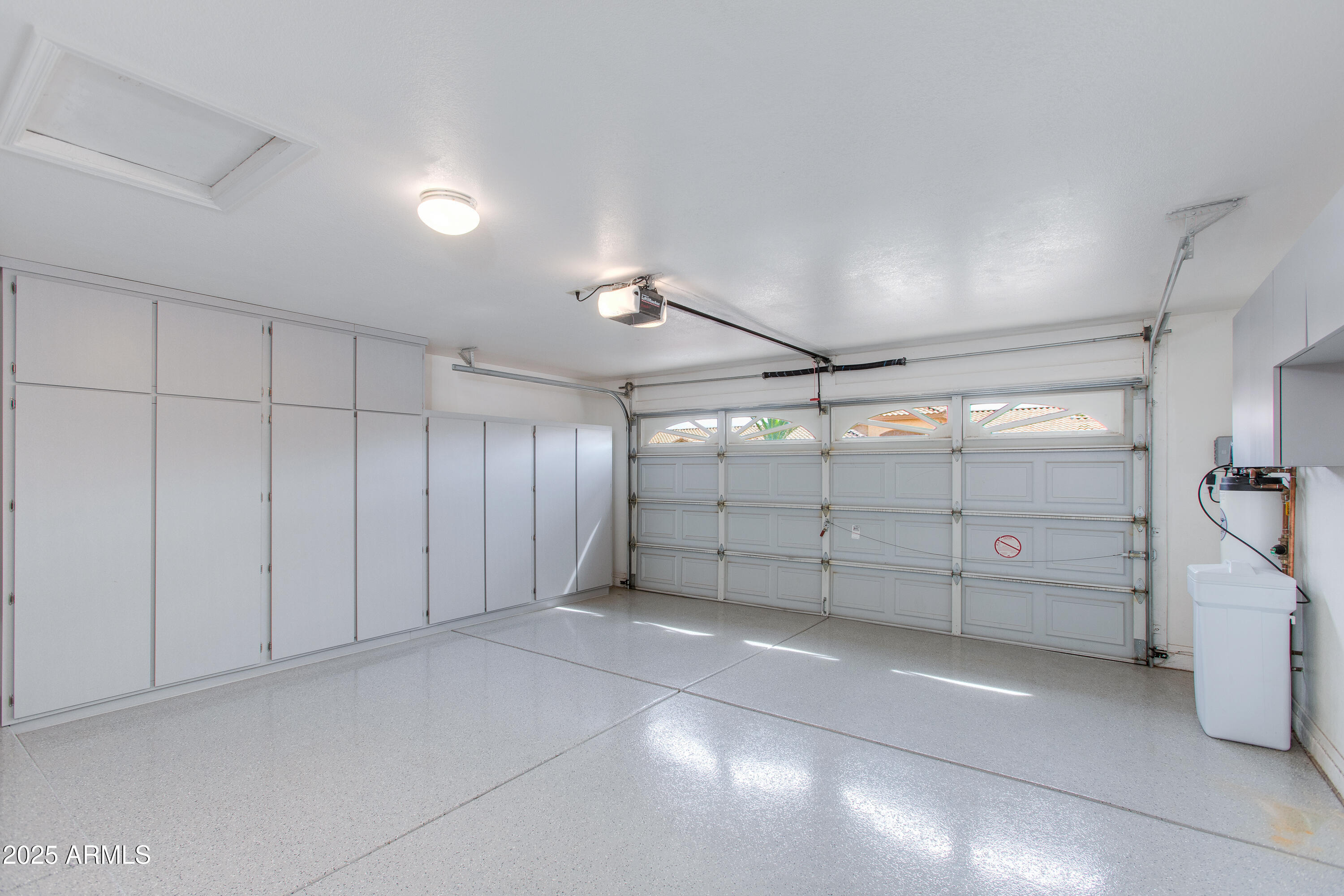 Empty garage with extensive white storage cabinets, a glossy speckled floor, and a utility sink.