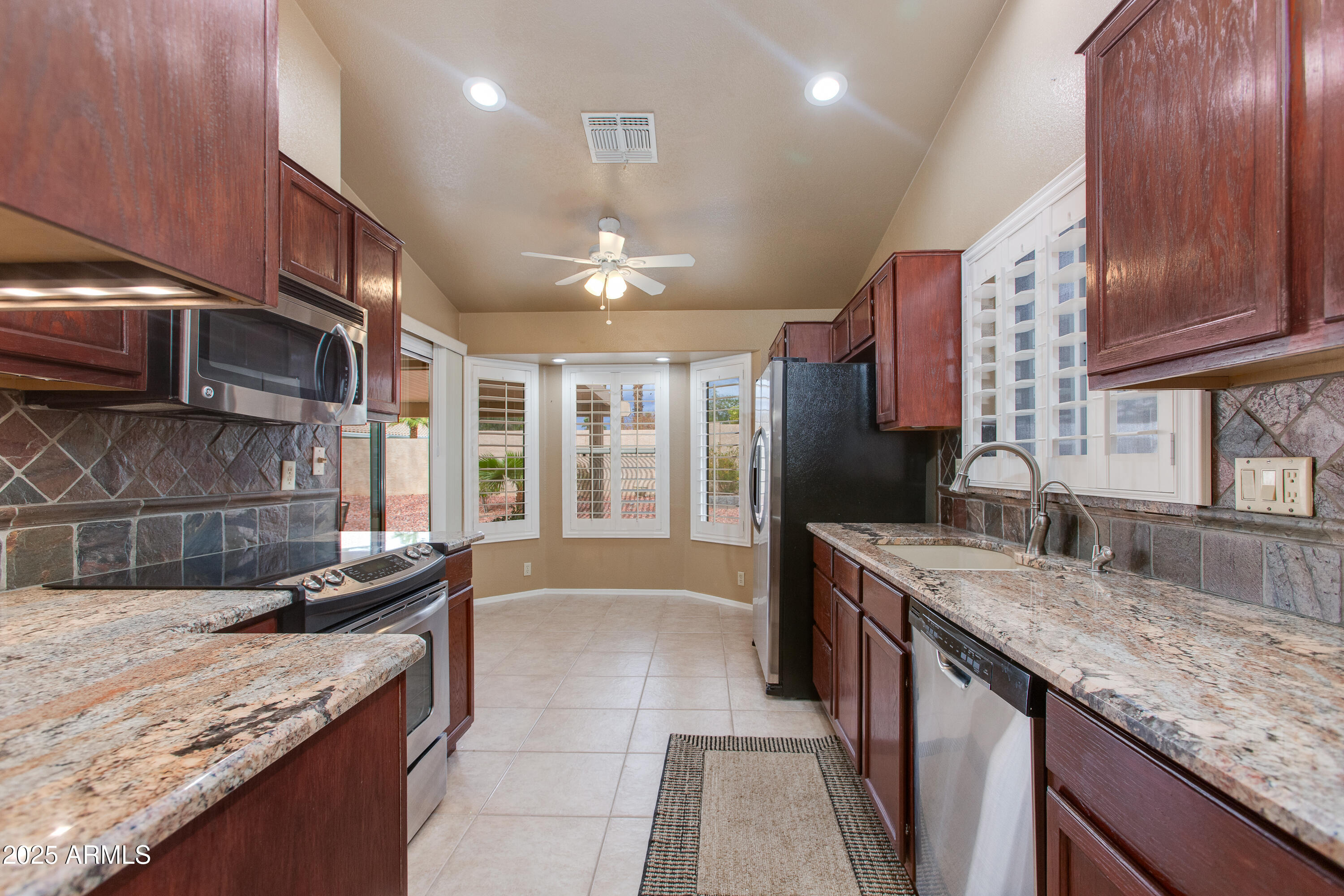 Galley kitchen with dark wood cabinets, granite counters, tile backsplash, and shuttered windows.