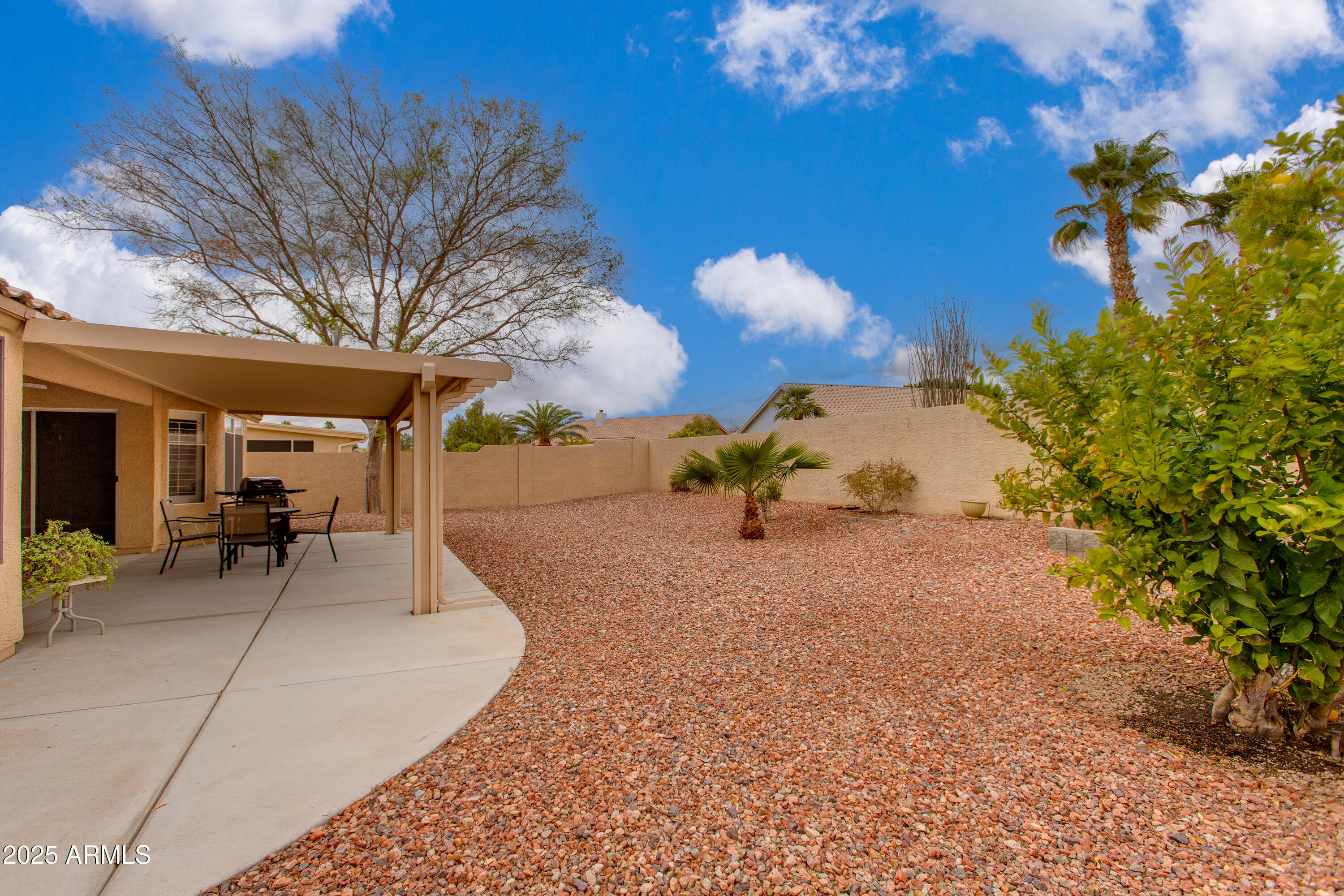 Backyard with a covered patio, outdoor dining set, reddish gravel landscaping, and a small palm.