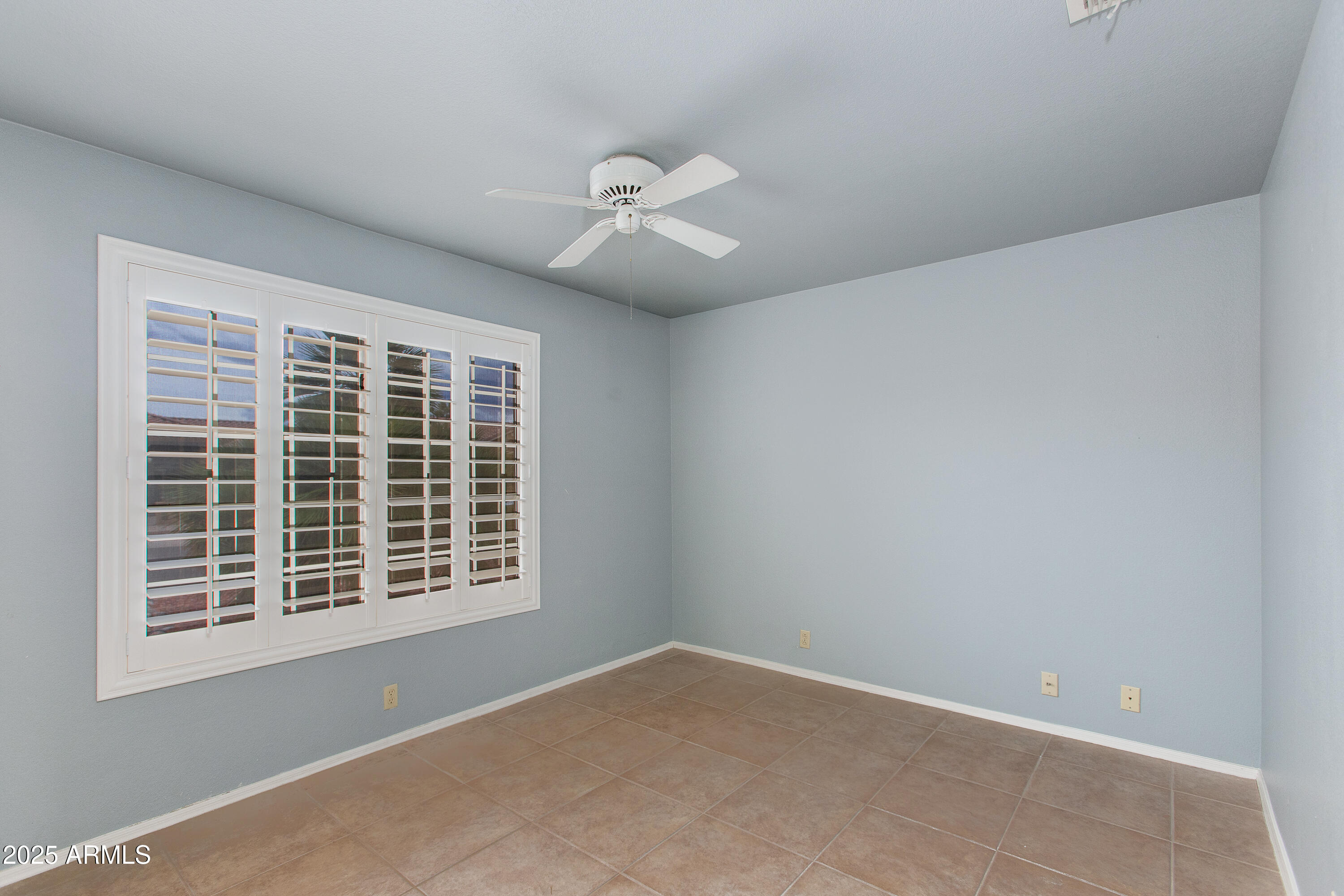 Empty room with plantation-shuttered windows, a white ceiling fan, and tan tile flooring.