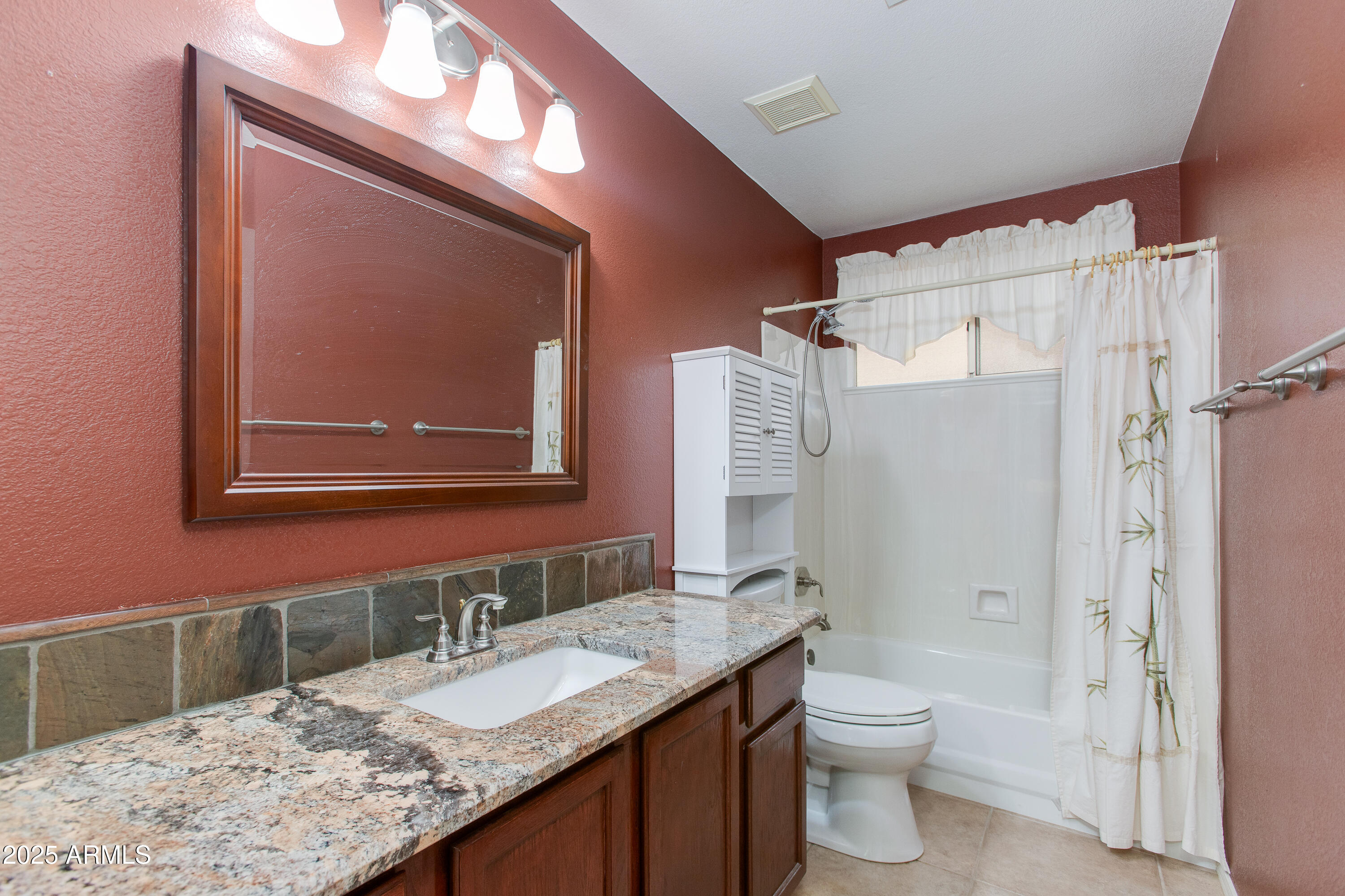 Bathroom with granite vanity, stone backsplash, and white tub-shower behind a curtain.