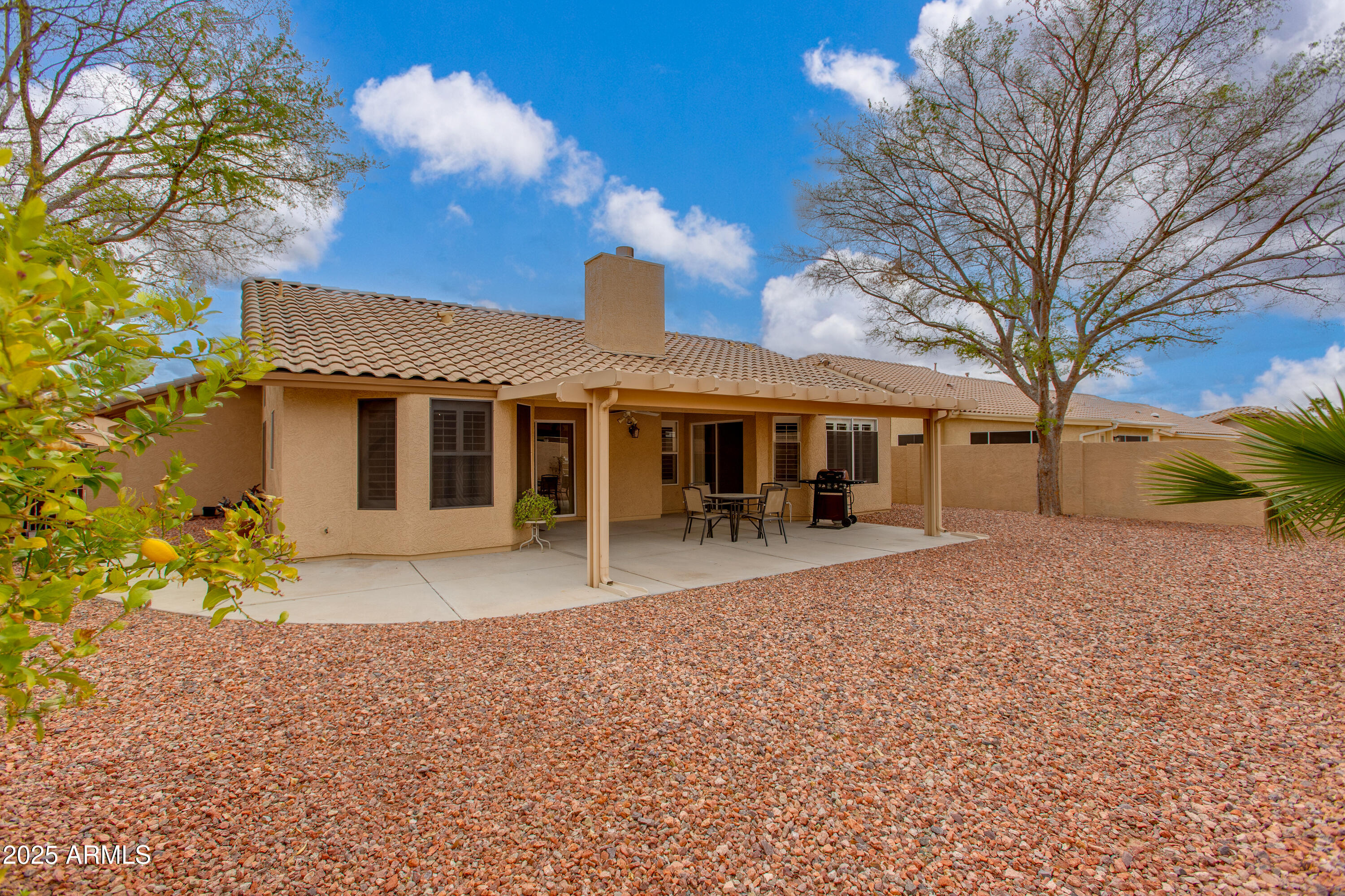 Home’s rear exterior with a covered patio, outdoor dining set, grill, and gravel landscaping.