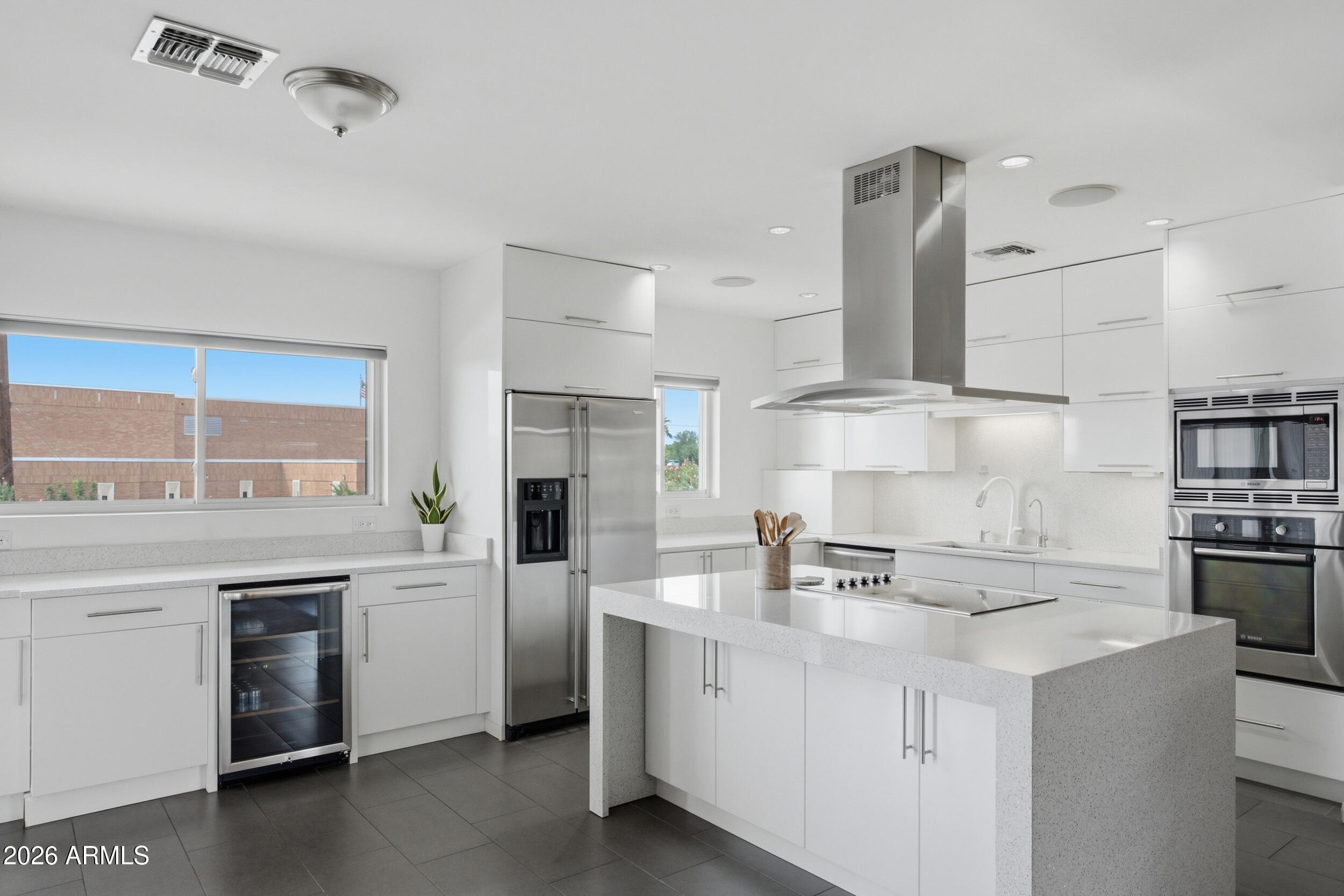 Modern white kitchen with a large cooktop island, stainless-steel appliances, and wide windows.