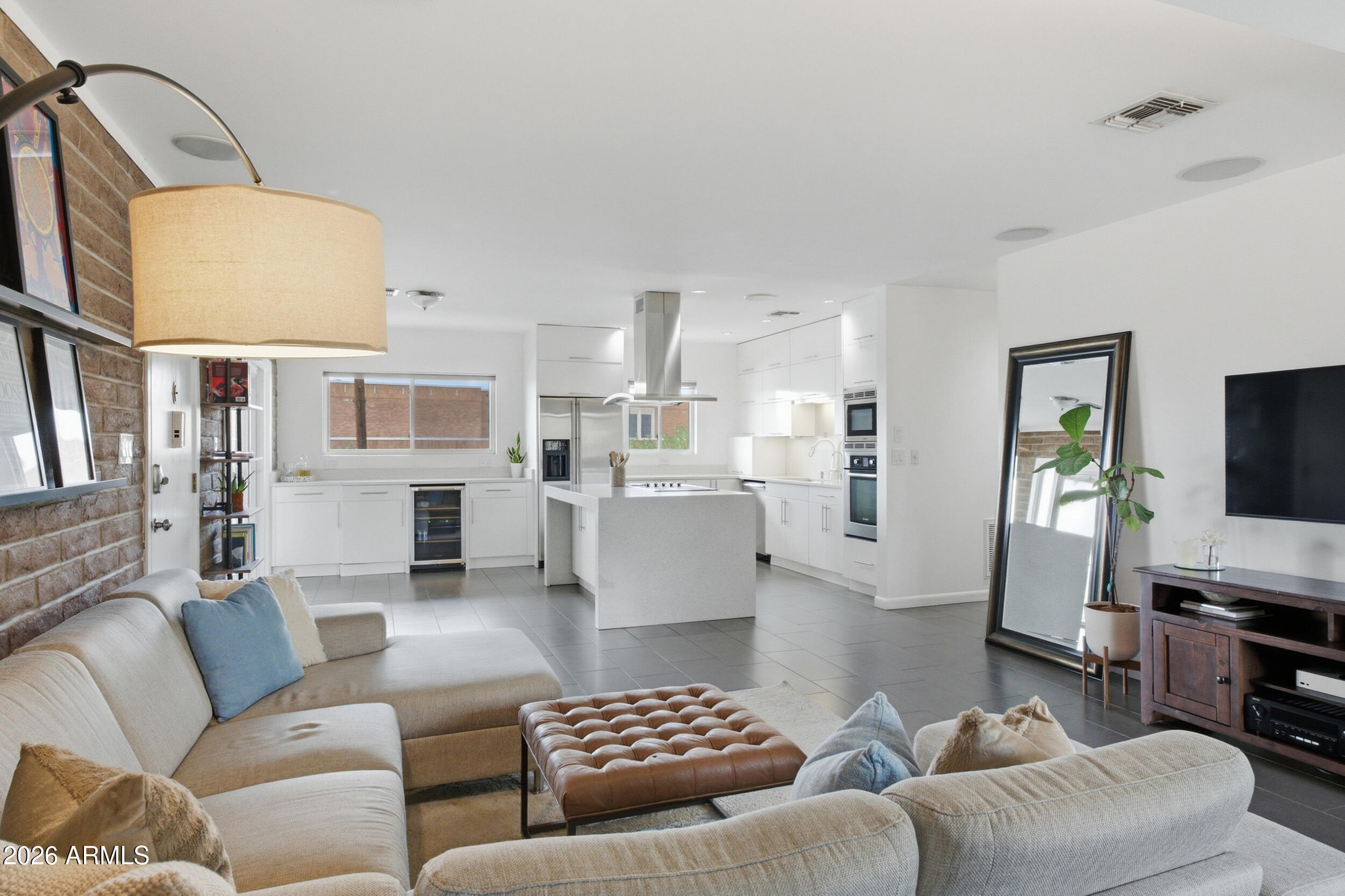 Open-plan living room and kitchen with a large white island, sectional sofa, and brick accent wall.