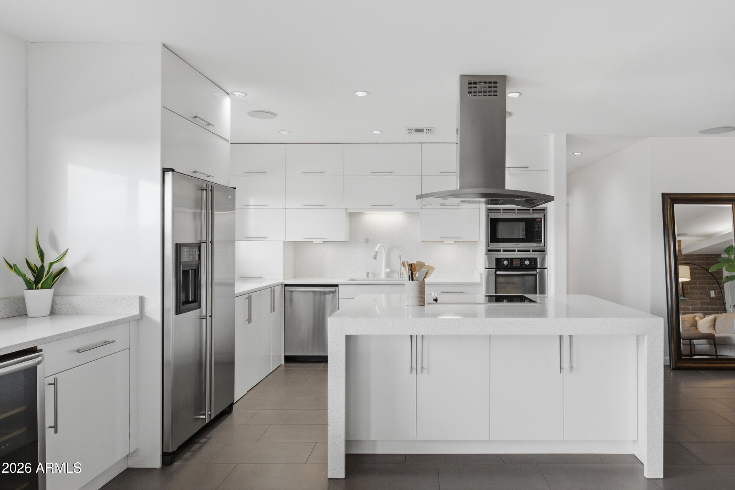 Modern white kitchen with a large island, stainless steel appliances, and gray tile floors.
