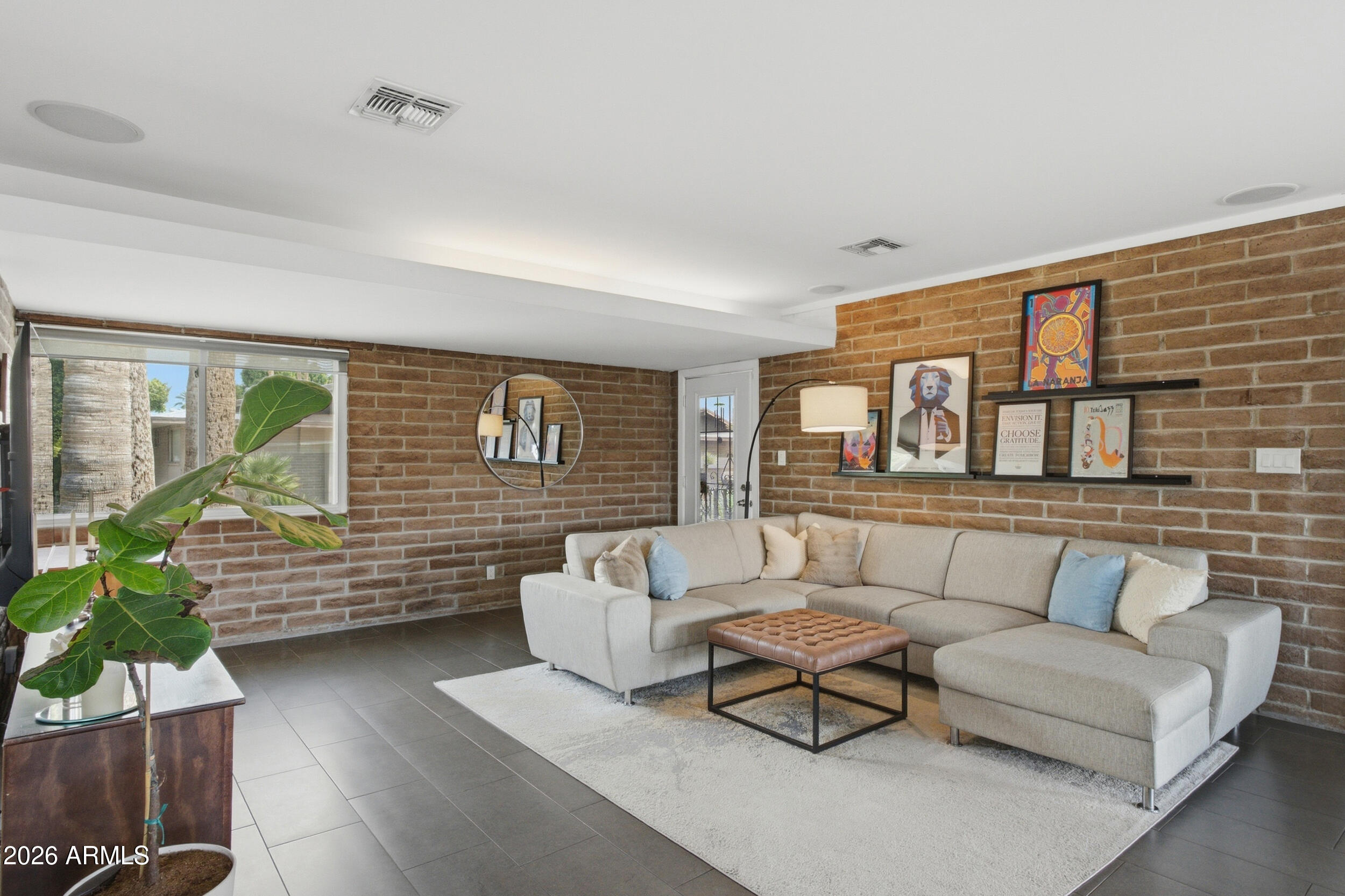 Living room with exposed brick walls, a light sectional sofa, and a large window beside a leafy plant.