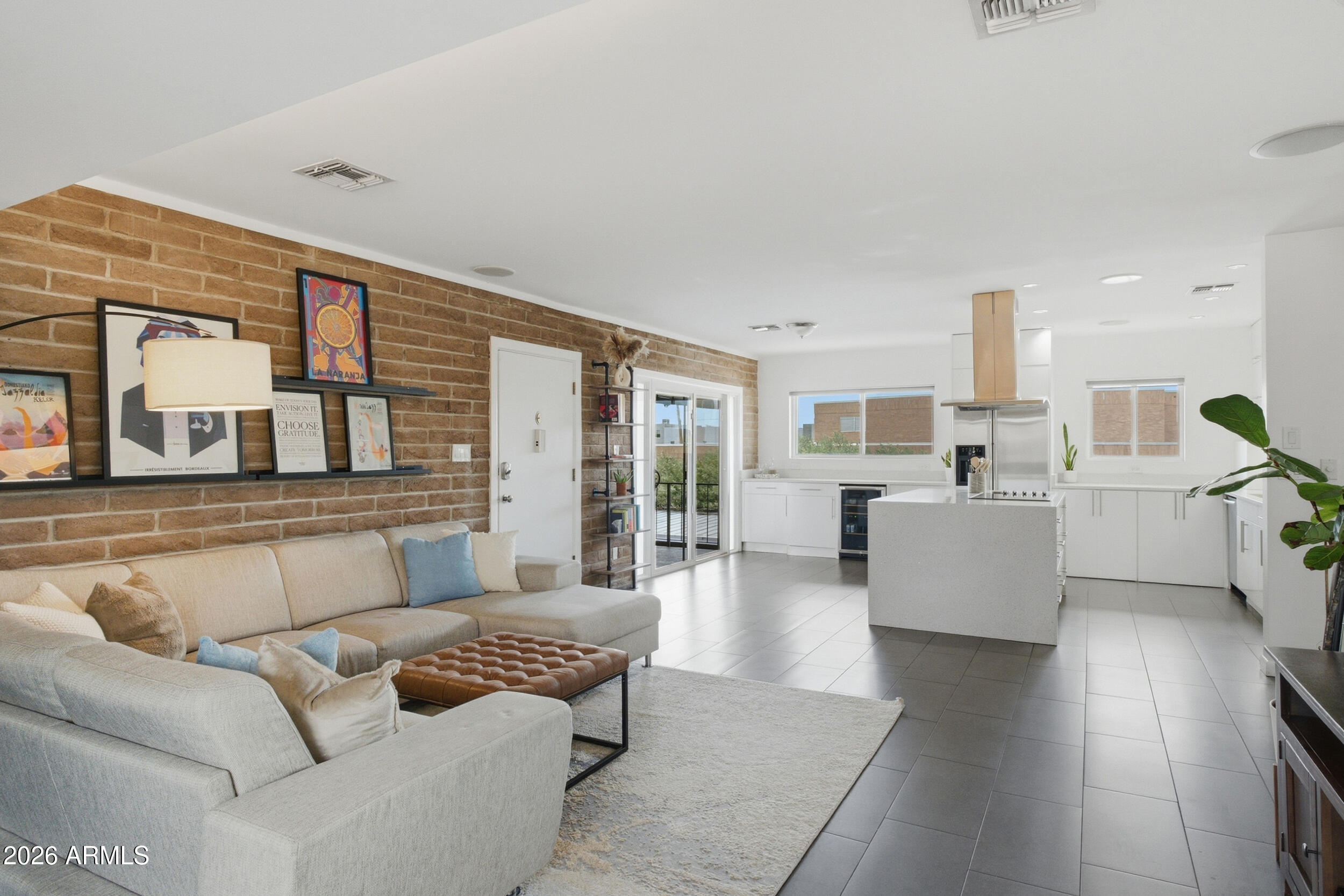 Open-plan living room and kitchen with a brick accent wall, sectional sofa, and white island.