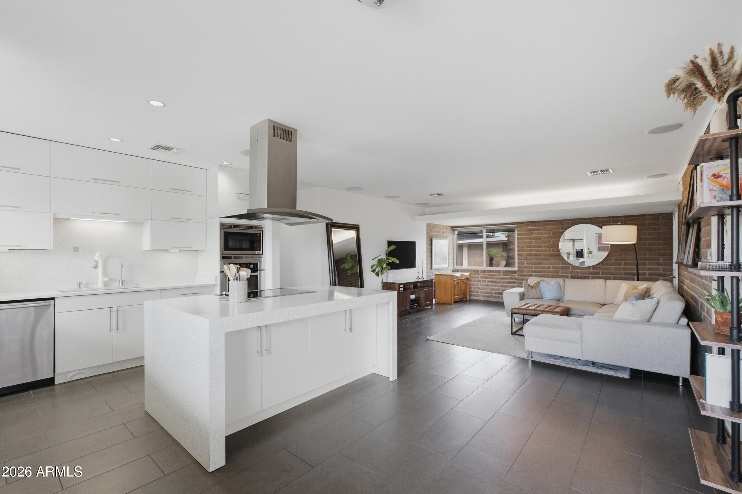 Open-plan kitchen and living room with a white island, sectional sofa, and exposed brick walls.
