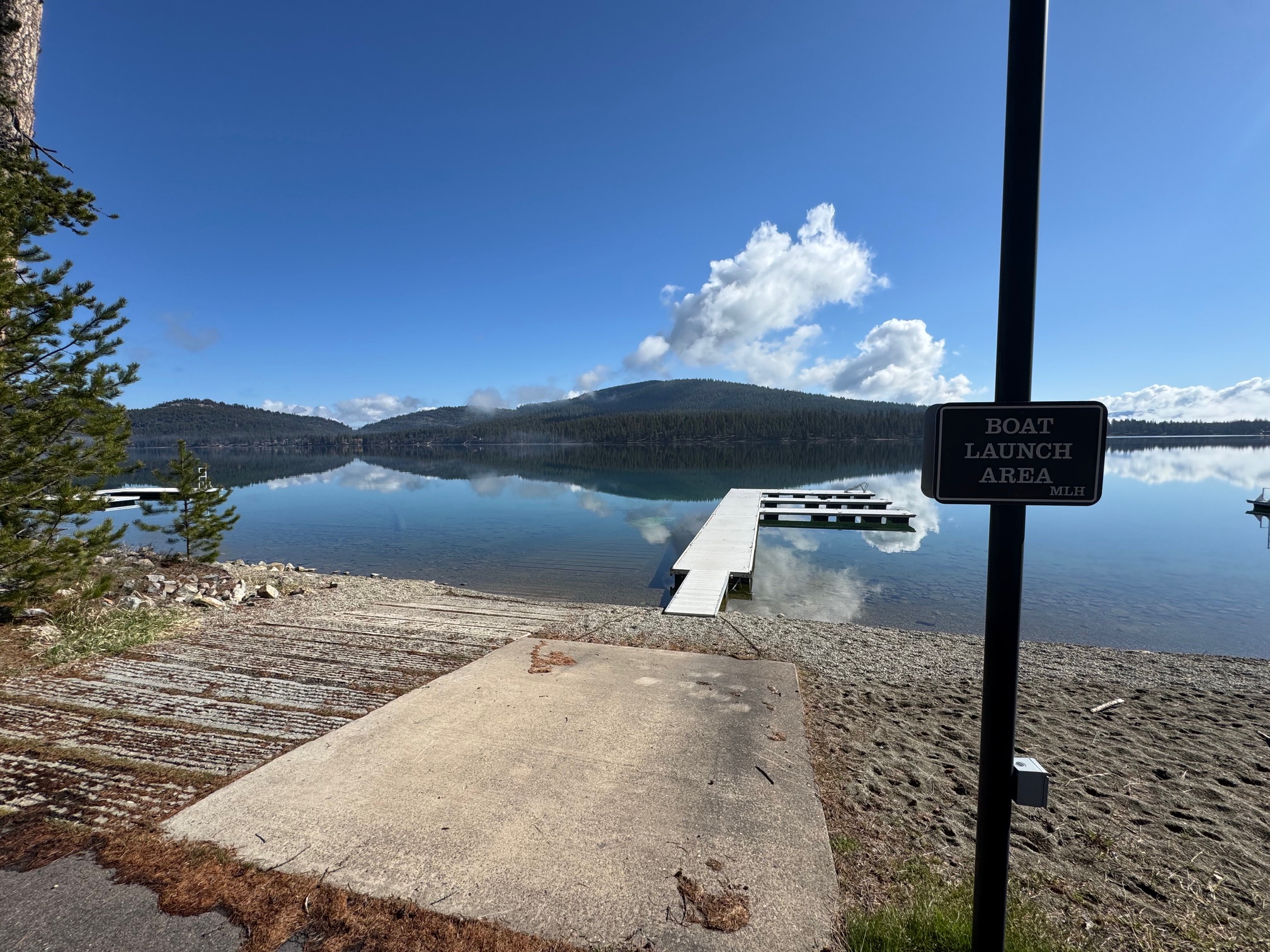 Boat launch ramp and floating dock on a calm lake, with forested hills reflected in the water.