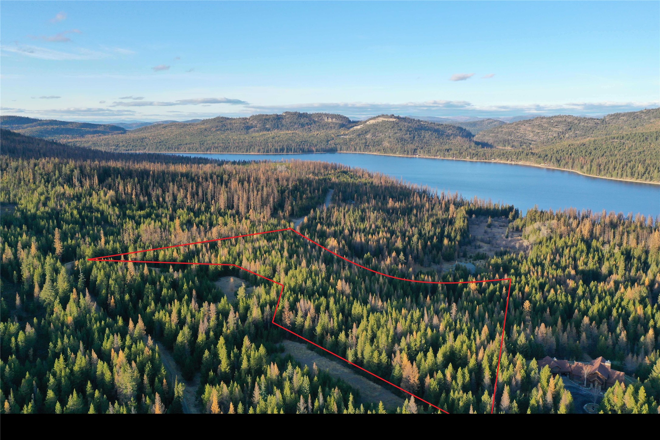 Aerial view of a wooded parcel outlined in red, with a lake and forested hills beyond.