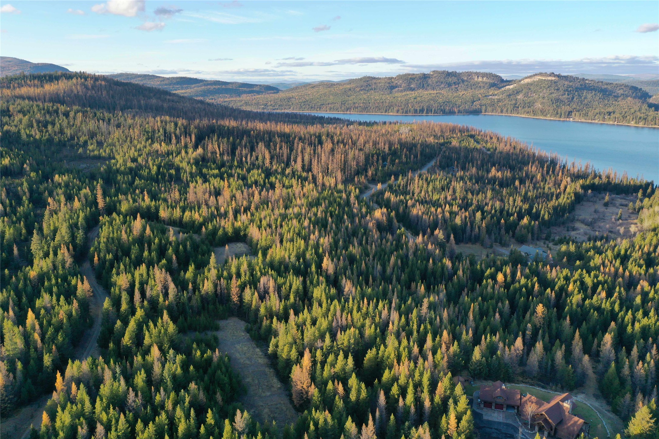 Aerial view of a forested property and large house beside a lake, surrounded by autumn-colored trees.