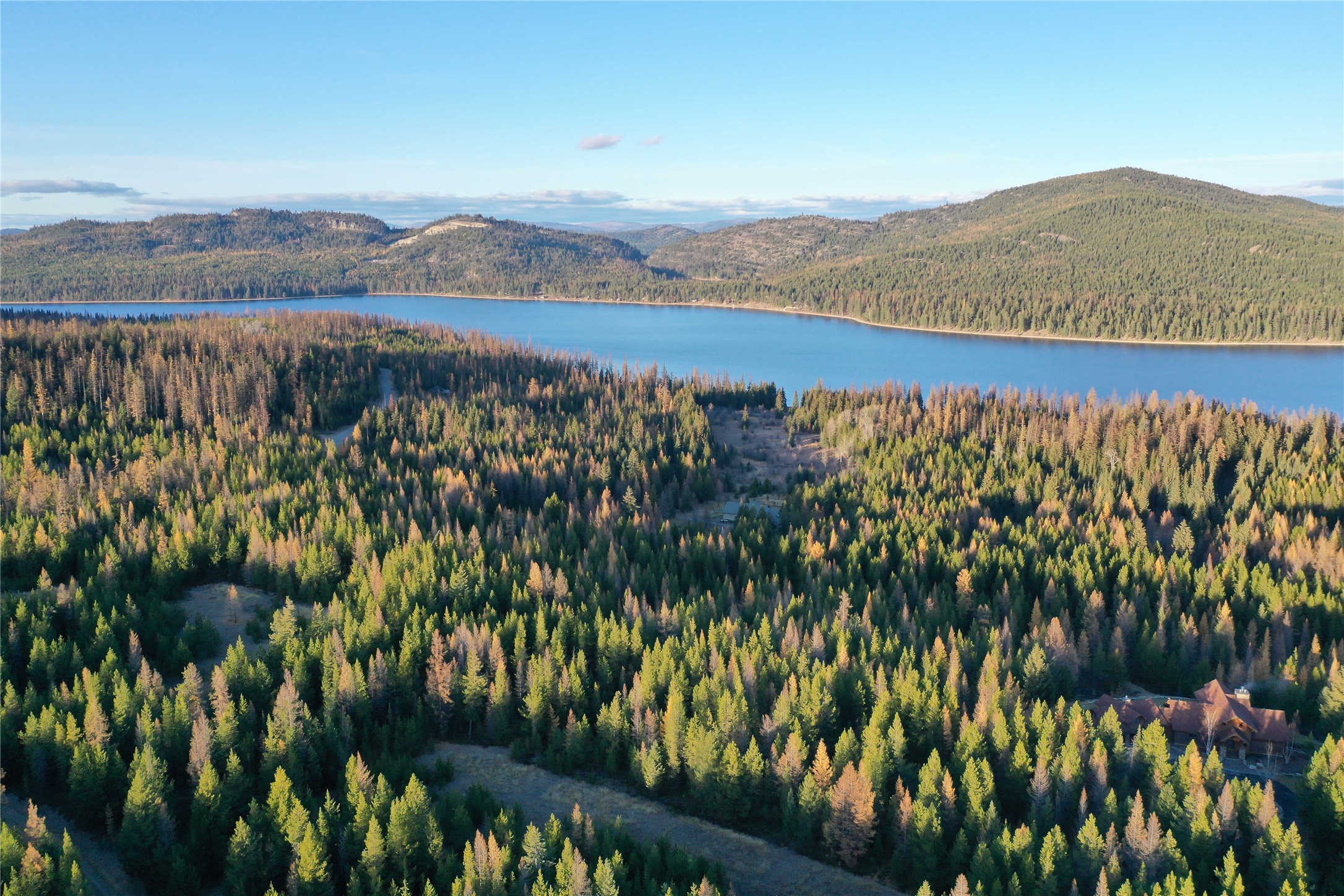 Aerial view of forested property beside McGregor Lake, with a cabin and wooded hills beyond.