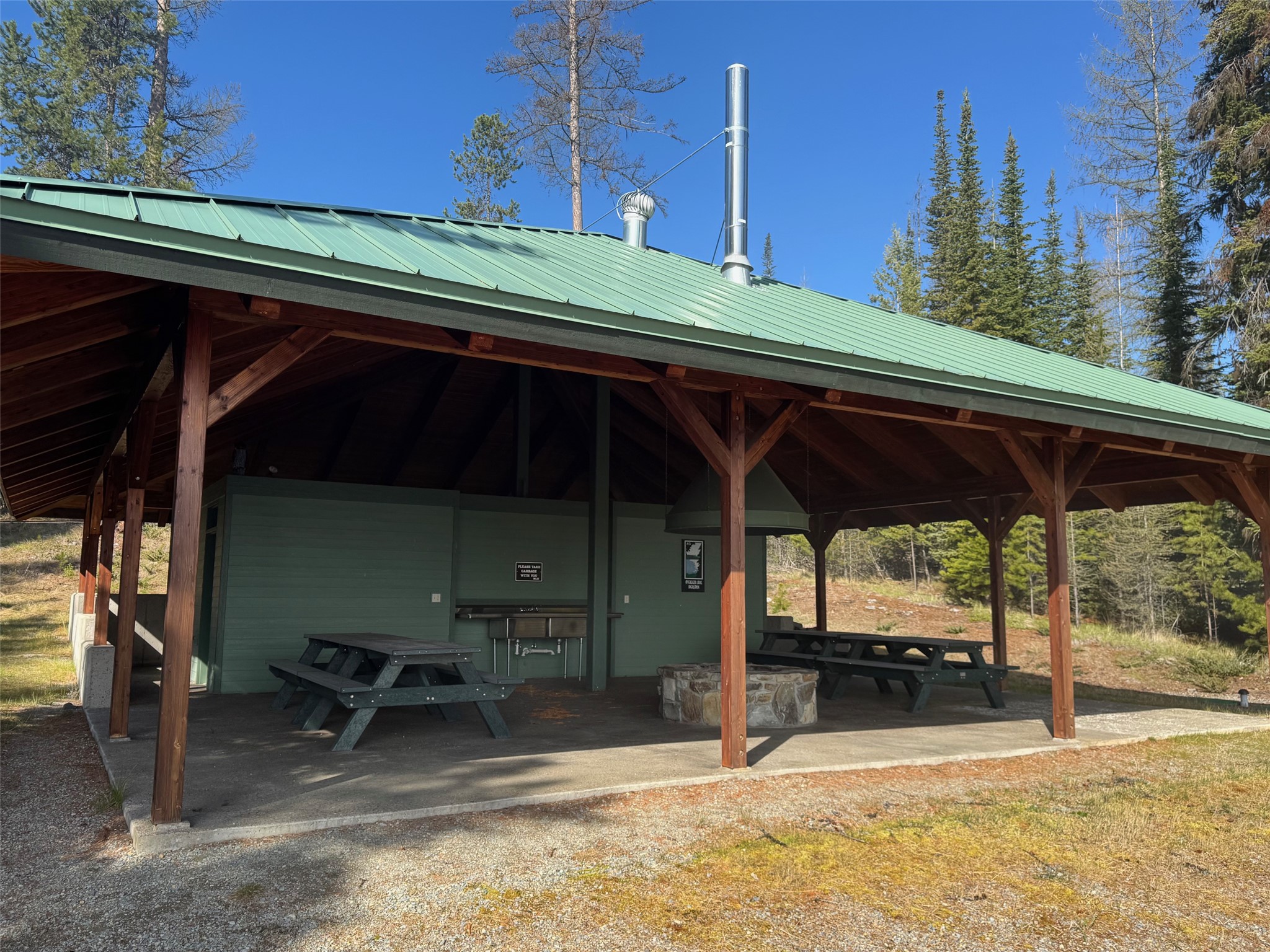 Covered timber pavilion with picnic tables, a built-in grill, and a stone fire ring.