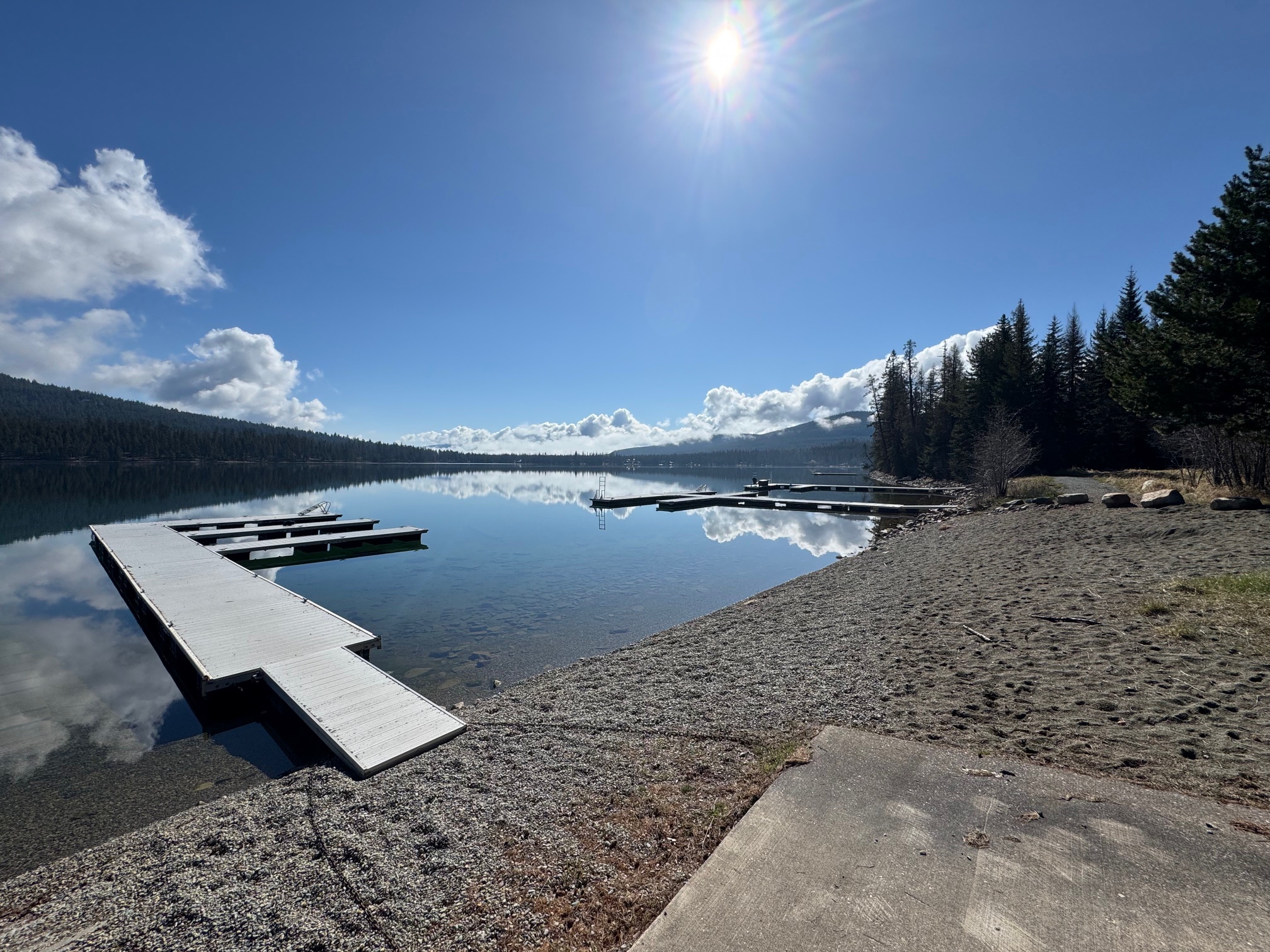 Calm lakefront with docks extending from a rocky beach, backed by evergreen forest.