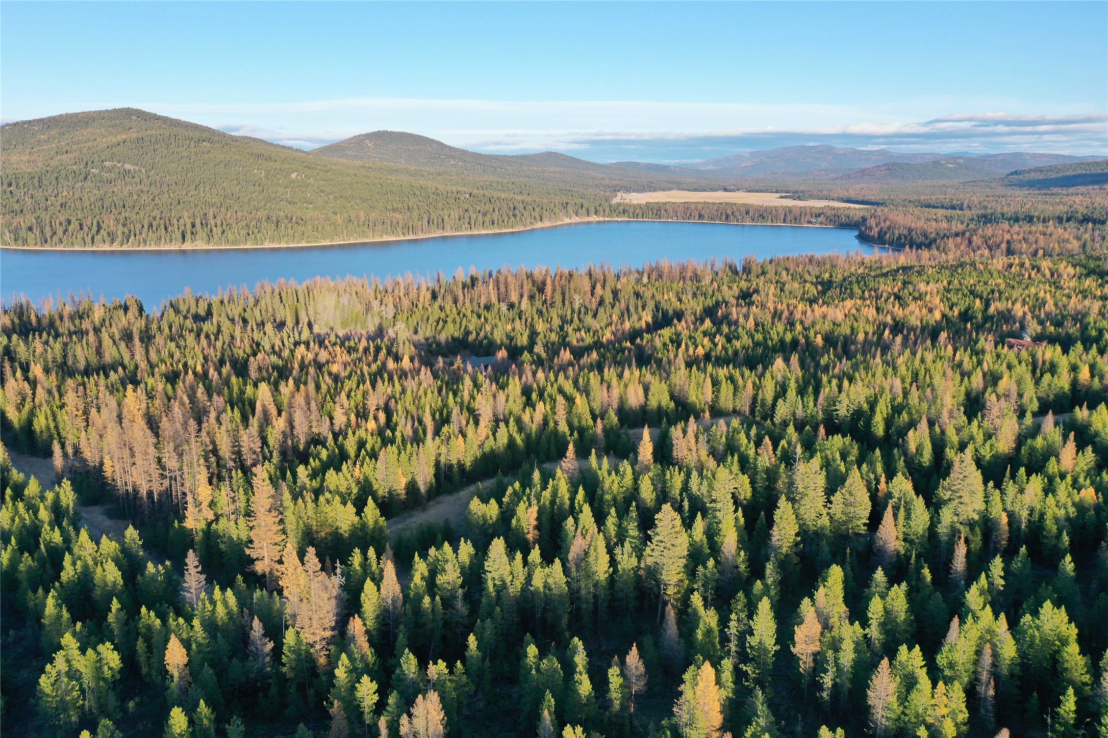 Aerial view of a lake surrounded by autumn-colored forest and rolling mountains.