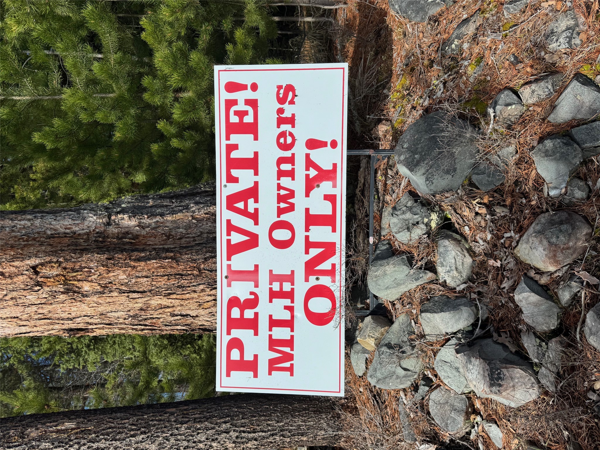 Private sign restricting access to MLH owners, set among pine trees and rocks.