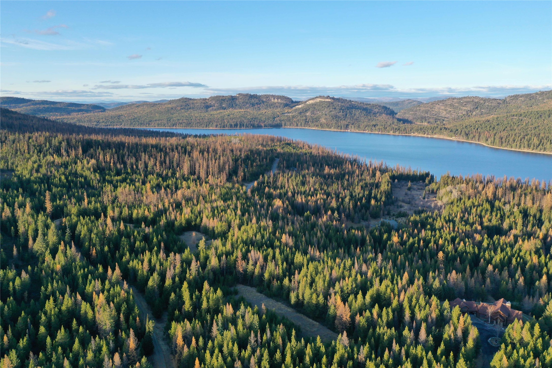 Aerial view of a lake and wooded hills, with a house nestled among autumn-colored trees.