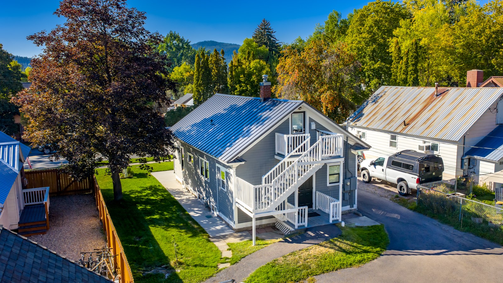 Gray two-story home with white exterior stairs and balconies, surrounded by autumn trees.