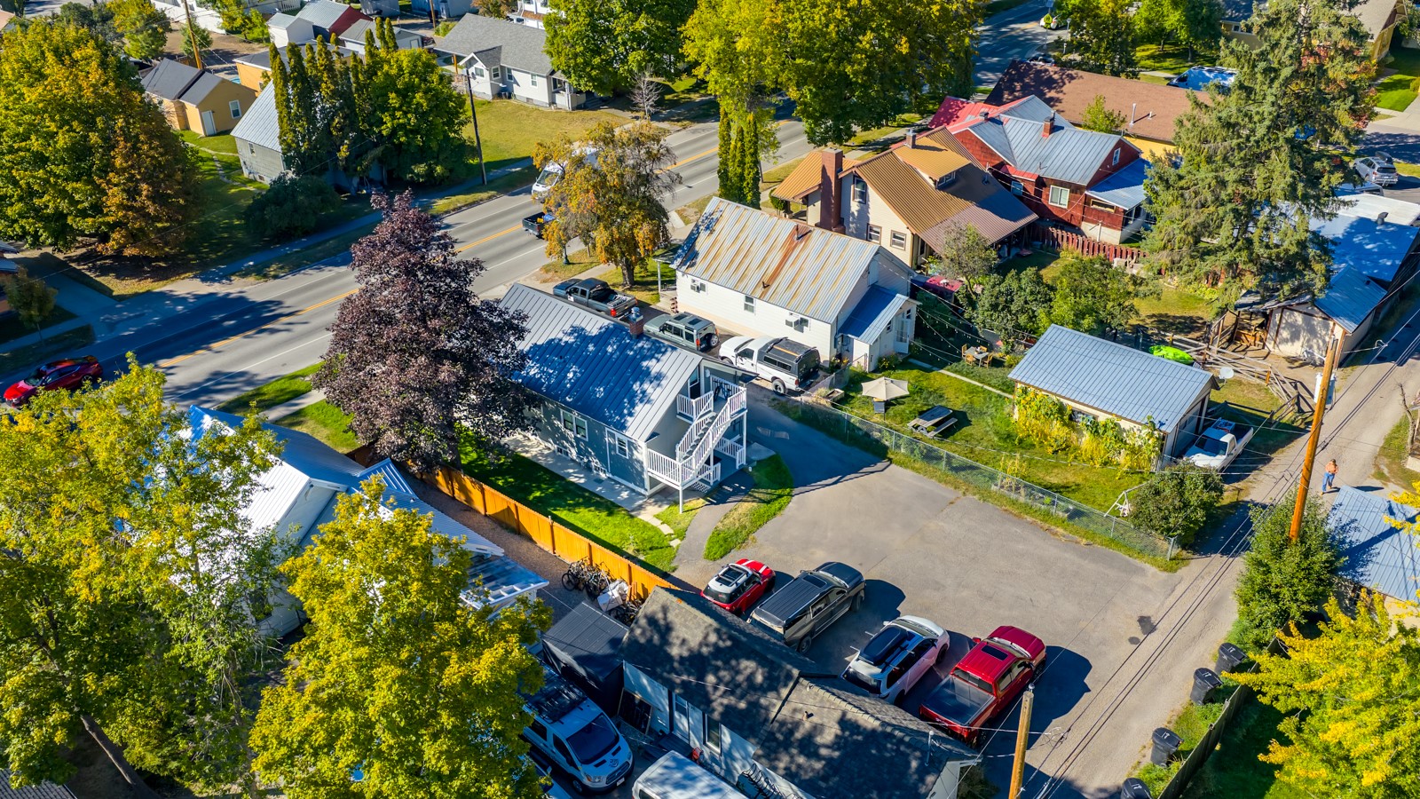 Aerial view of a blue-gray home with a white porch beside a shared parking area.