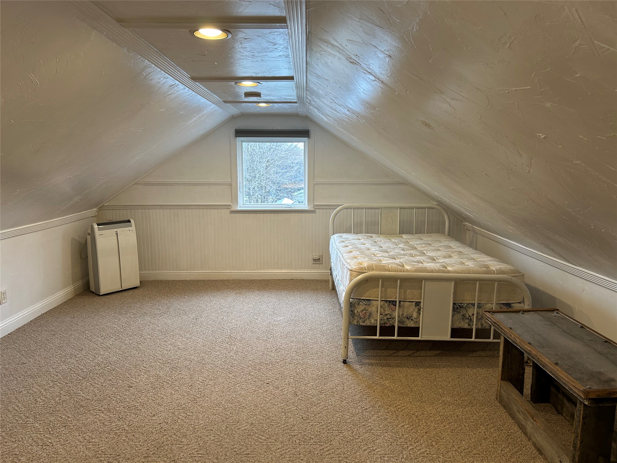Attic bedroom with a metal bed, sloped ceiling, and small window.