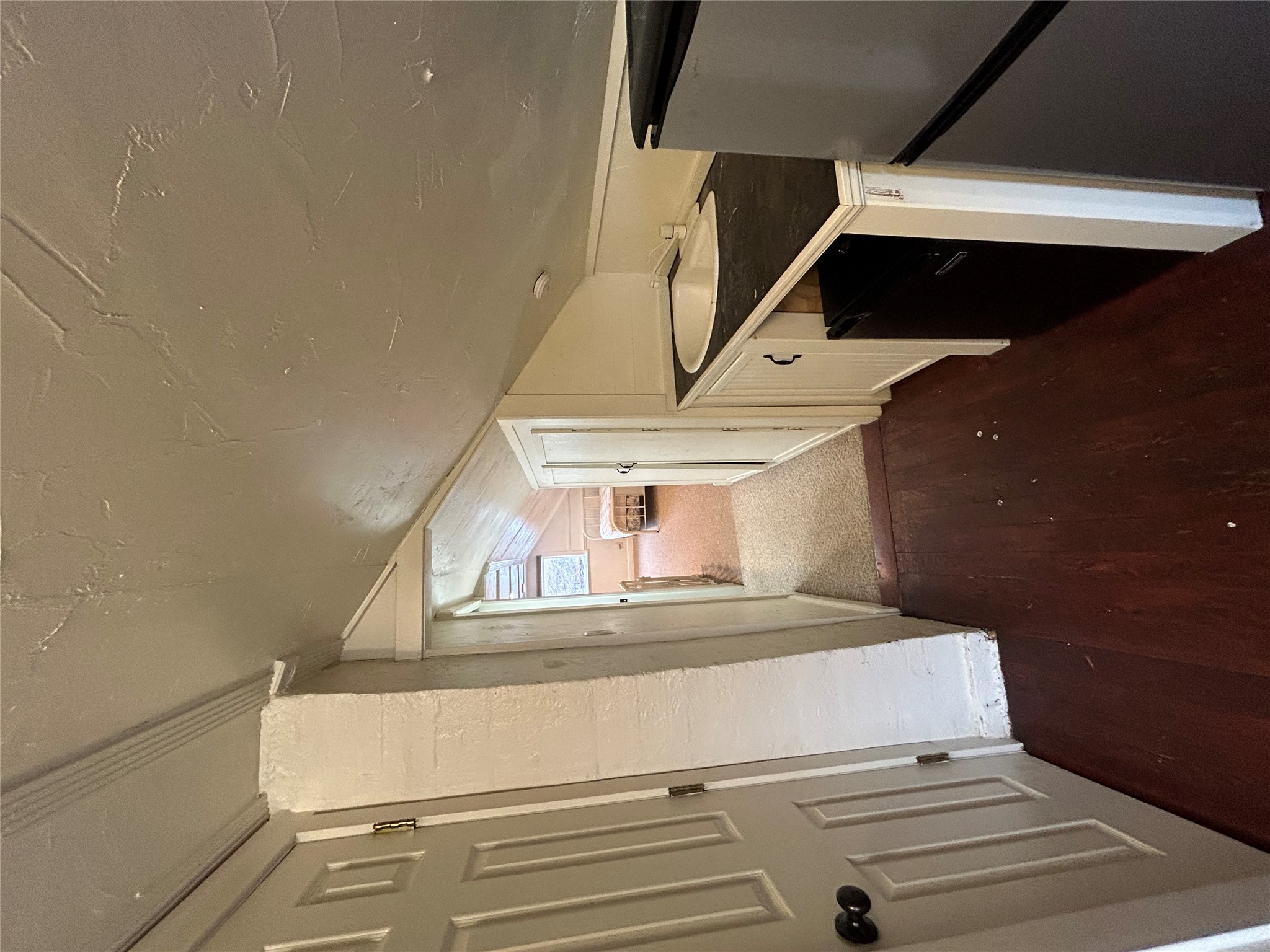 Narrow attic kitchenette with a sink and refrigerator, opening onto a small bedroom with a bed.