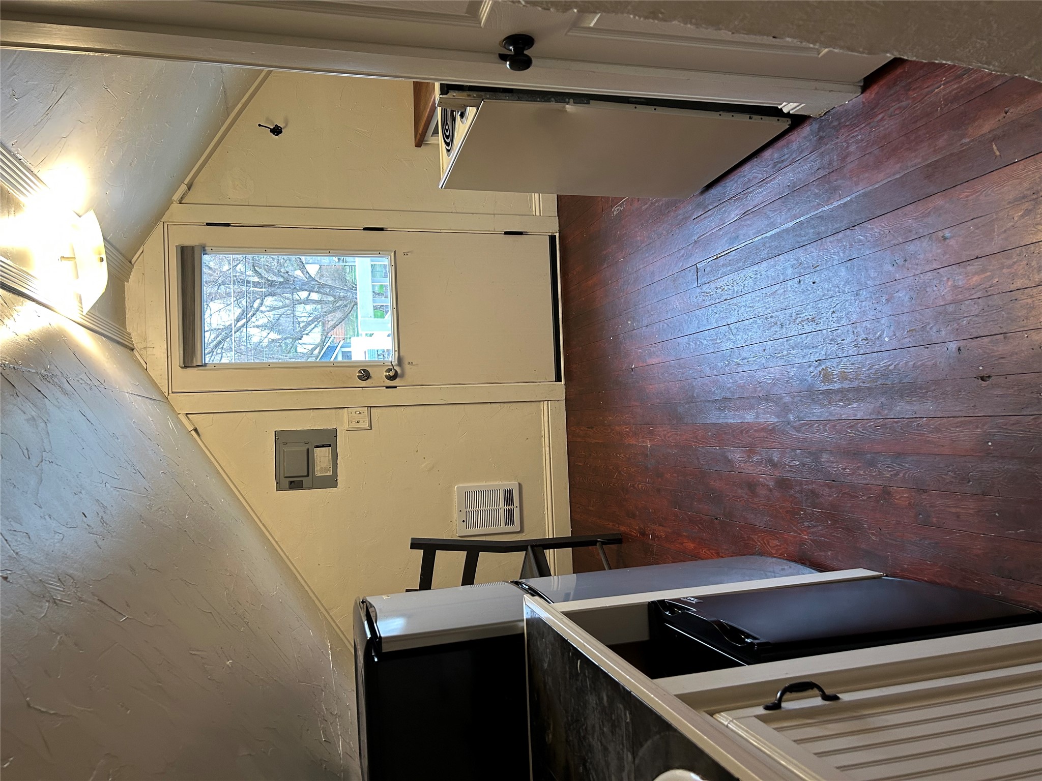 Compact kitchen beneath a sloped ceiling, with a windowed door and dark wood floors.