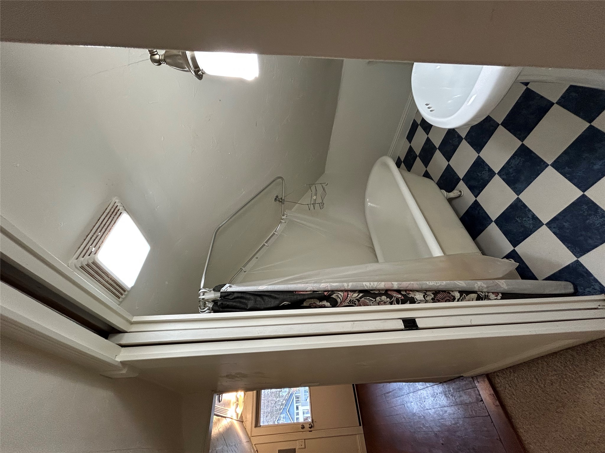 Bathroom with a clawfoot tub beneath a sloped ceiling and black-and-white checkerboard floor.