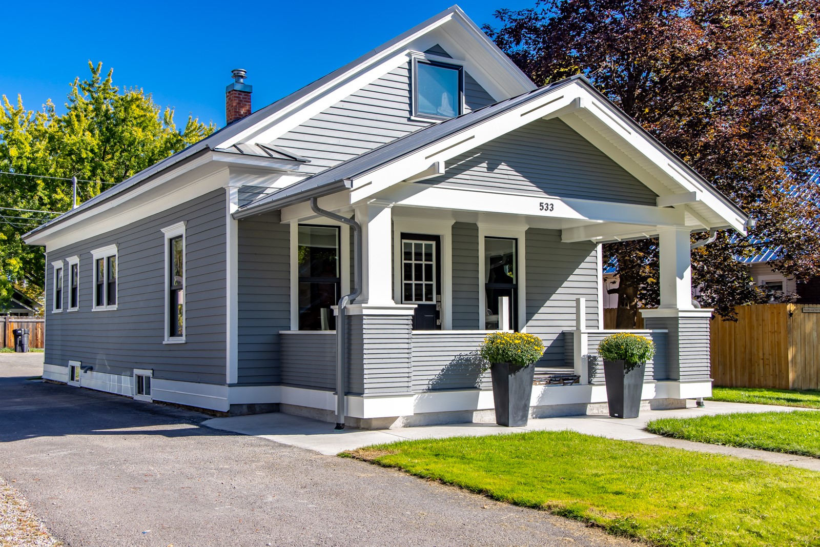 Gray house with white trim, a covered front porch, and two potted plants.