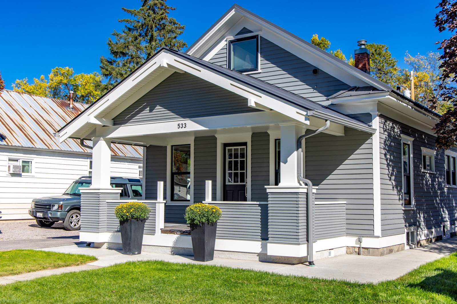 Gray house with white trim, a covered porch, and flower planters beside the entrance.