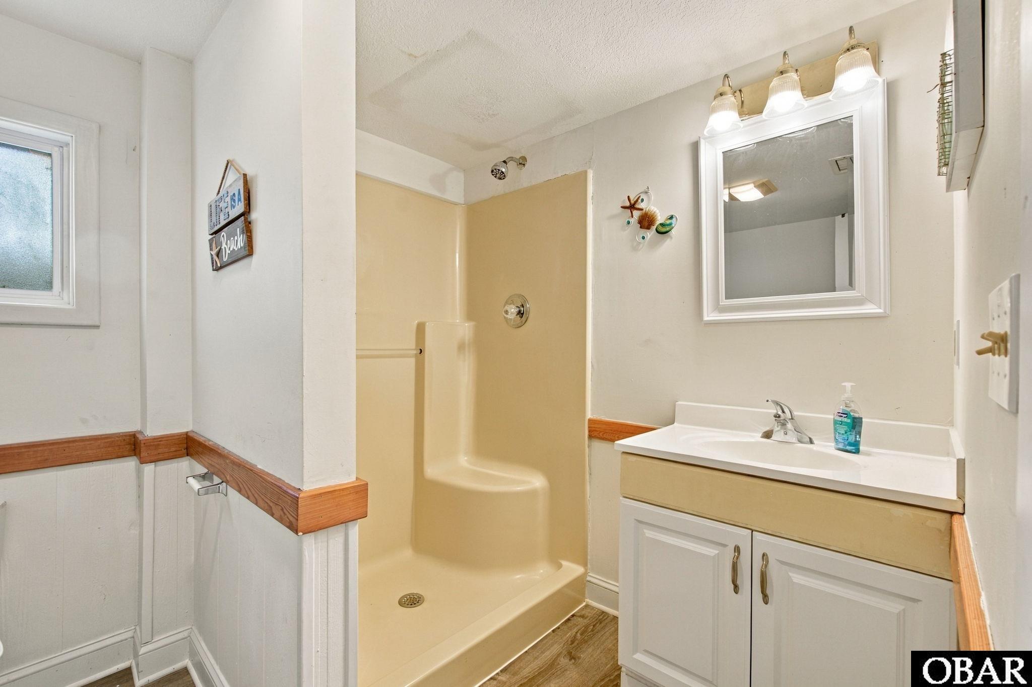 Bathroom with a beige walk-in shower, white vanity, framed mirror, and wood trim.