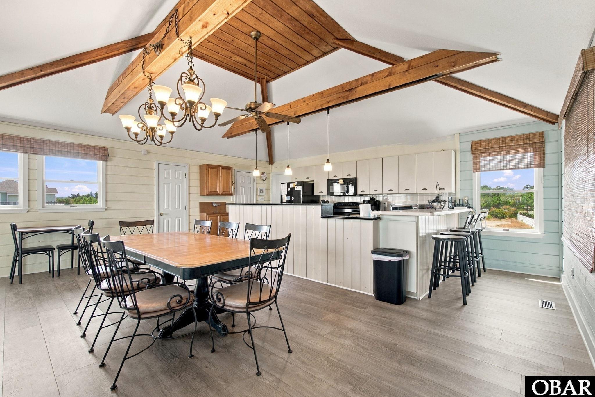 Open-plan kitchen and dining area with exposed timber beams, a long table, and a breakfast bar.