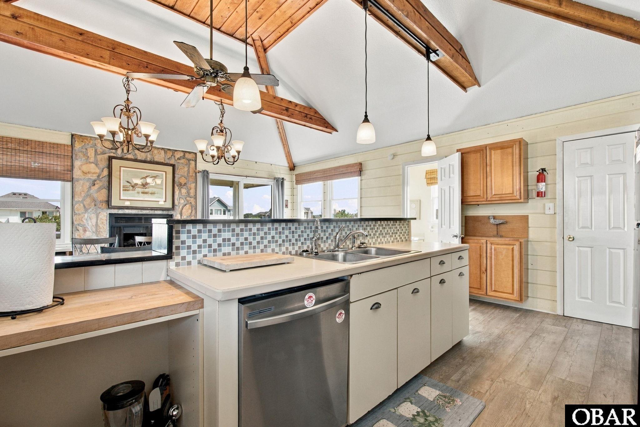 Kitchen with a large island and mosaic backsplash beneath a vaulted ceiling with exposed wooden beams.