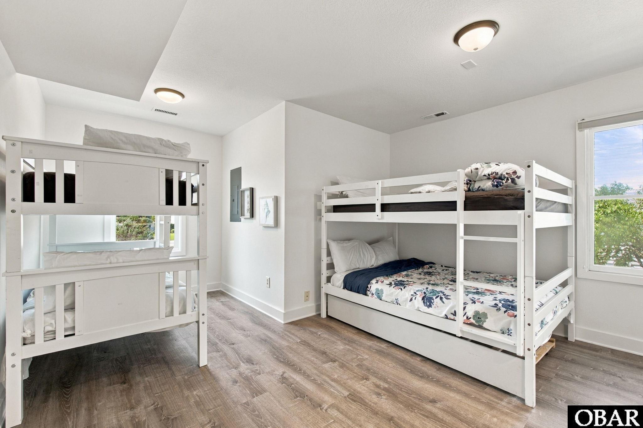 Bedroom with two white bunk beds, floral bedding, and gray wood-look flooring.