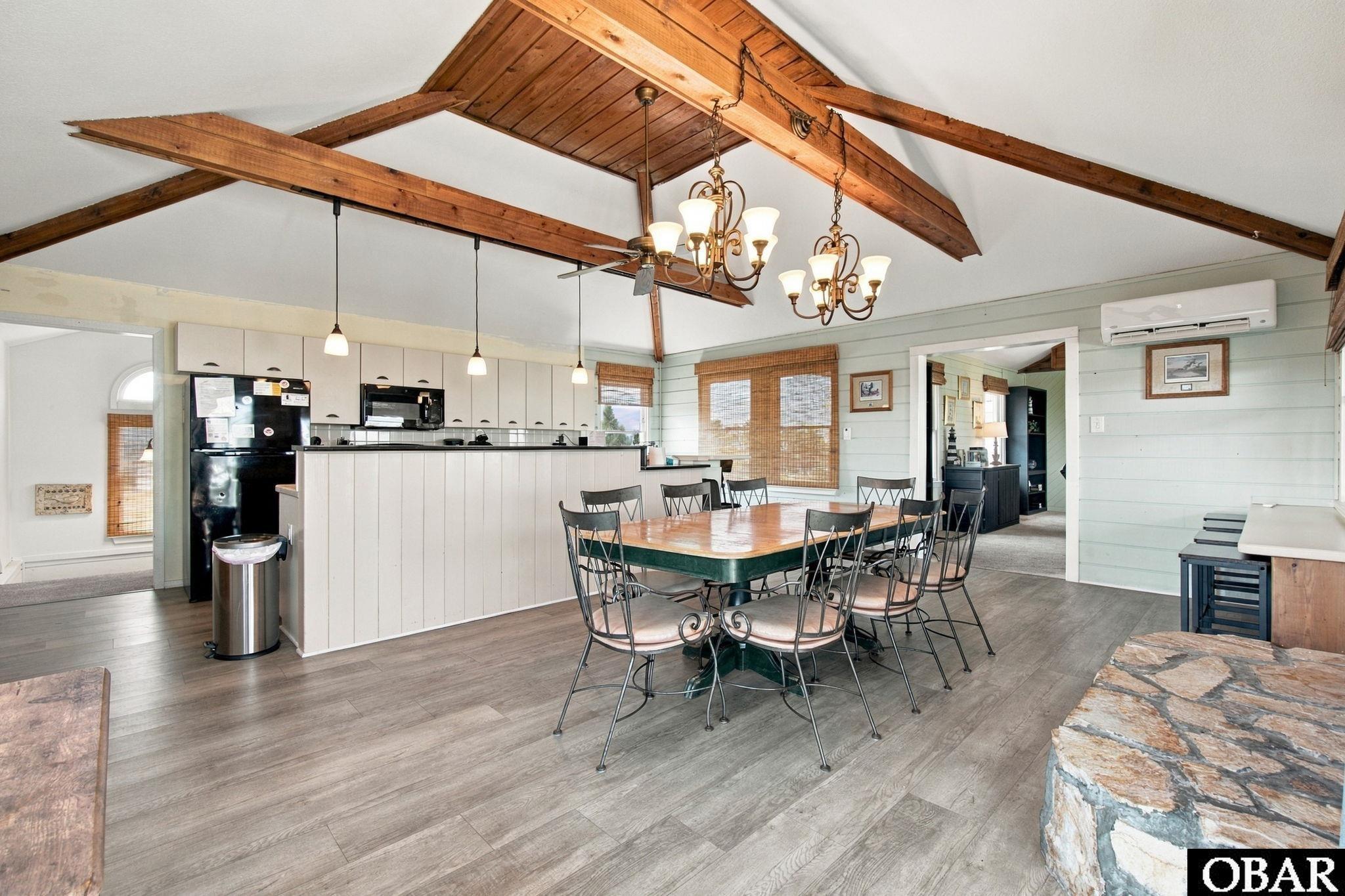 Kitchen and dining area with exposed wooden beams, a large table, and two chandeliers.