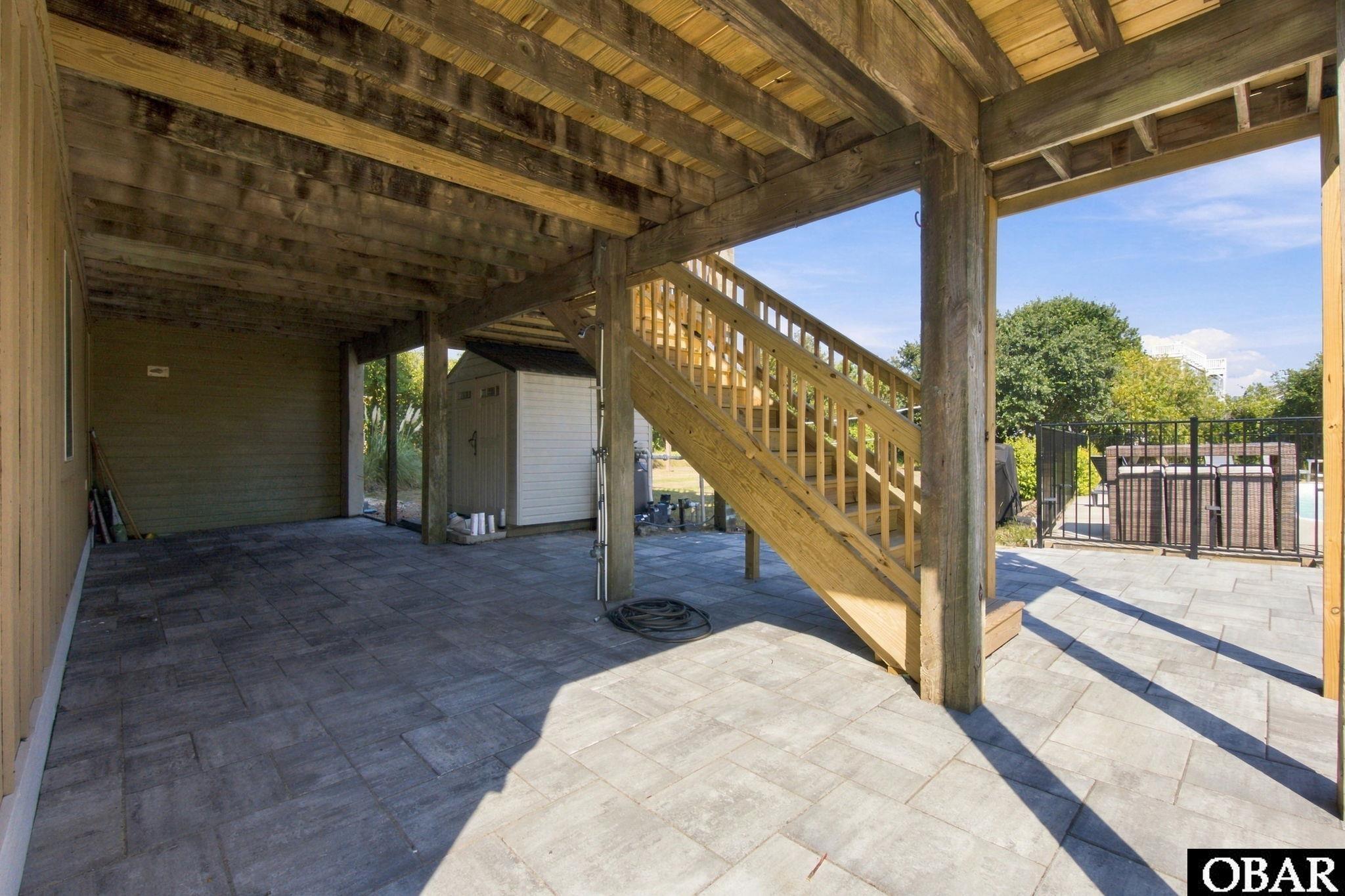 Covered patio with timber stairs and paver flooring beside a fenced swimming pool.