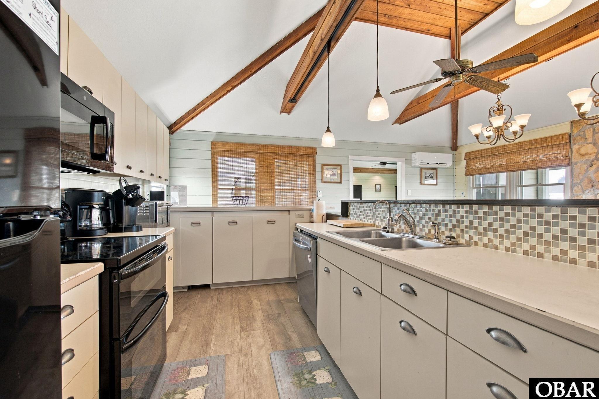 Kitchen with cream cabinets, double sink, tiled backsplash, and exposed wooden ceiling beams.