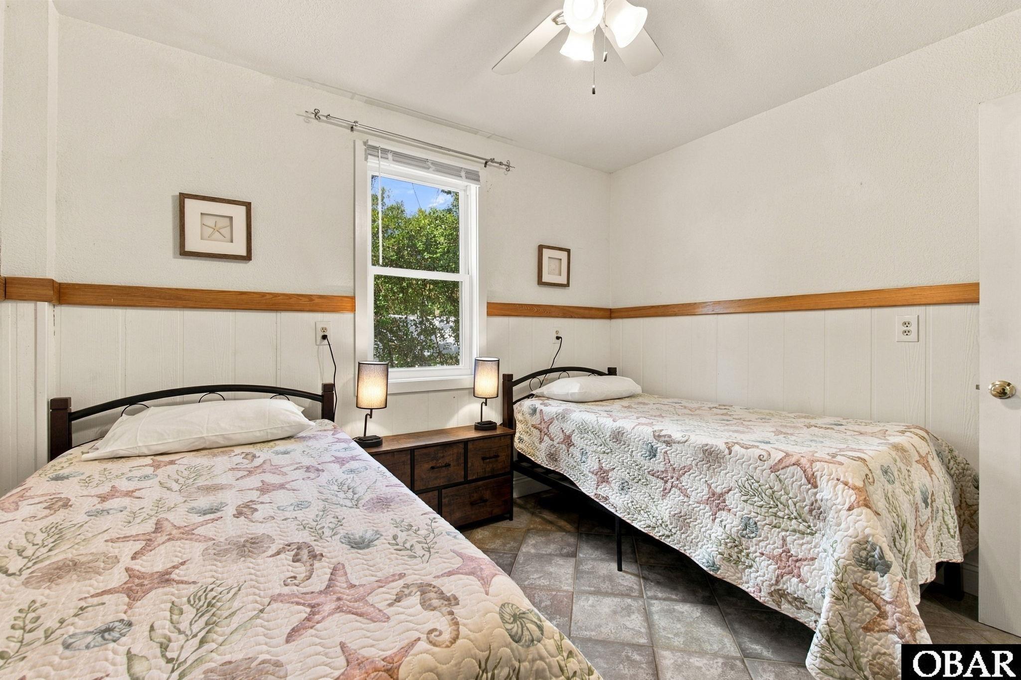 Bedroom with two seashell-patterned beds, a shared nightstand, and a window.