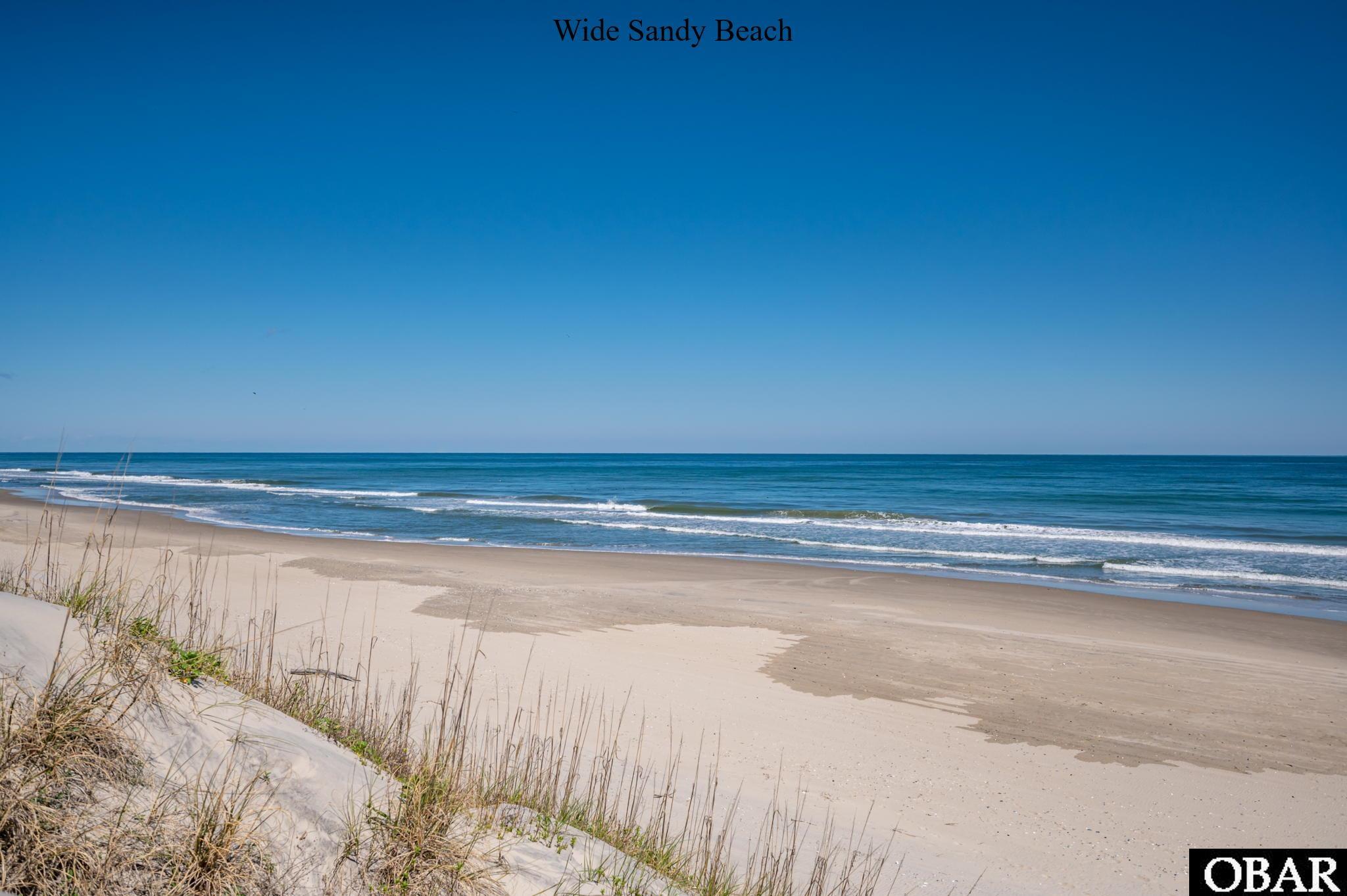 Wide sandy beach with dune grass in the foreground and gentle ocean waves.